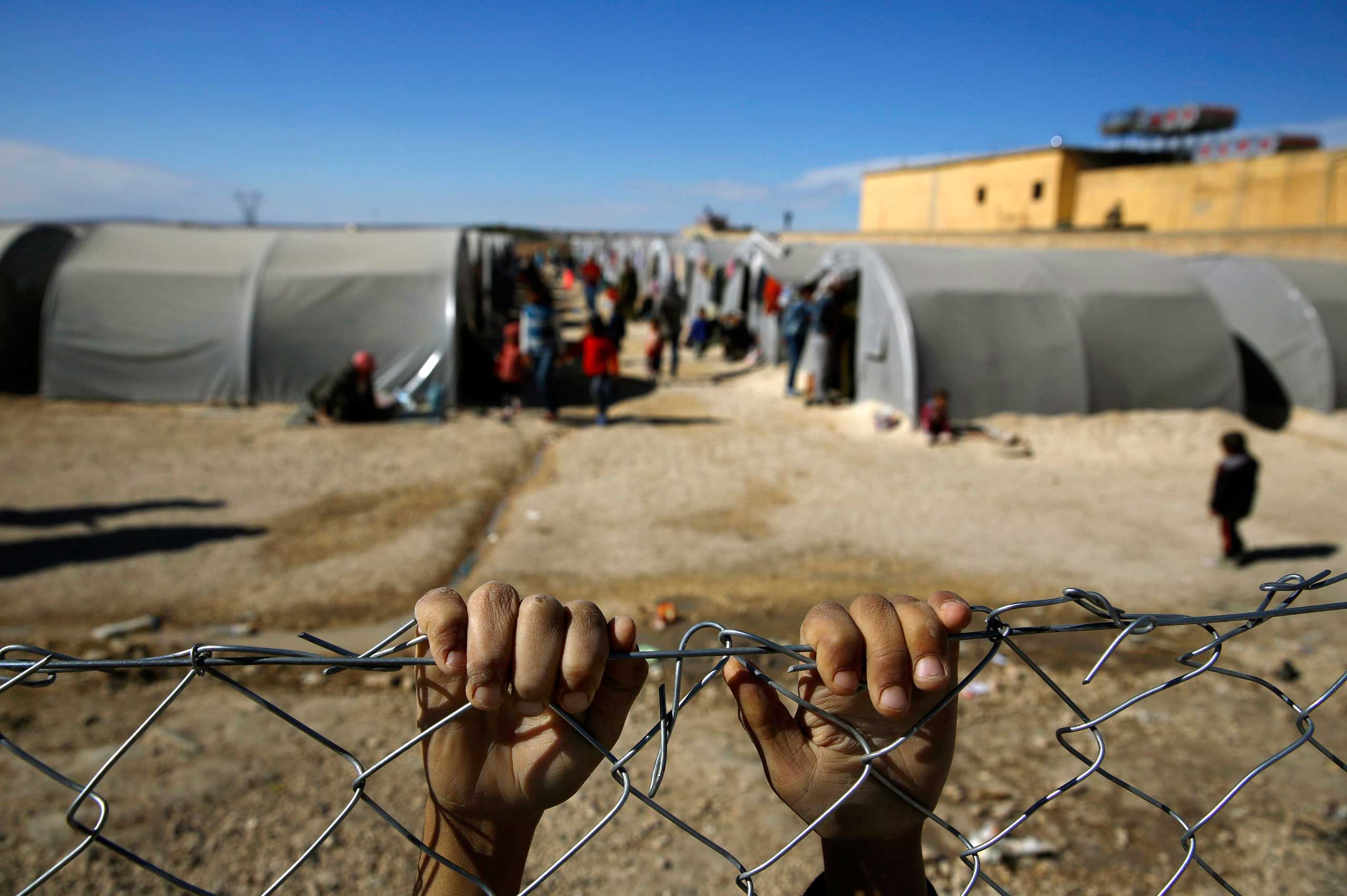 Kurdish refugee boy from the Syrian town of Kobani holds onto a fence that surrounds a refugee camp in the border town of Suruc, Sanliurfa province