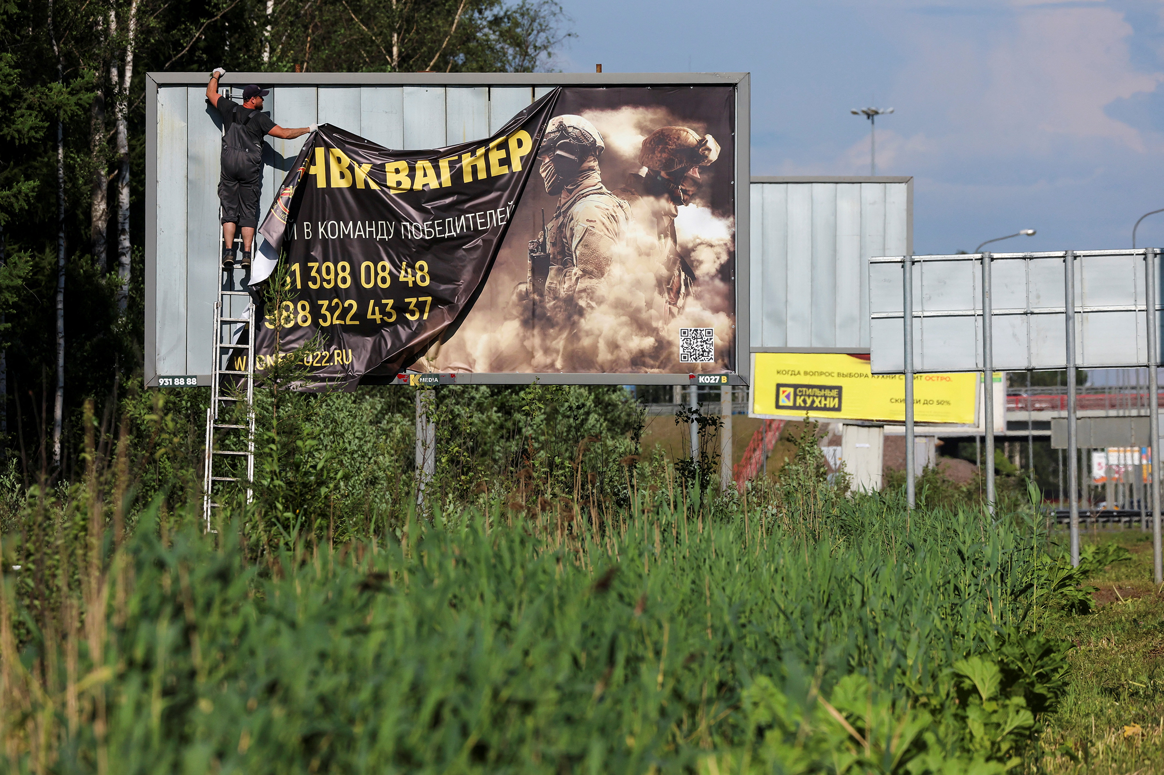 A worker removes an advertising banner promoting service in Wagner private mercenary group on the outskirts of Saint Petersburg, Russia, on June 24. A slogan on the banner reads: "Accede to the team of victors!" 