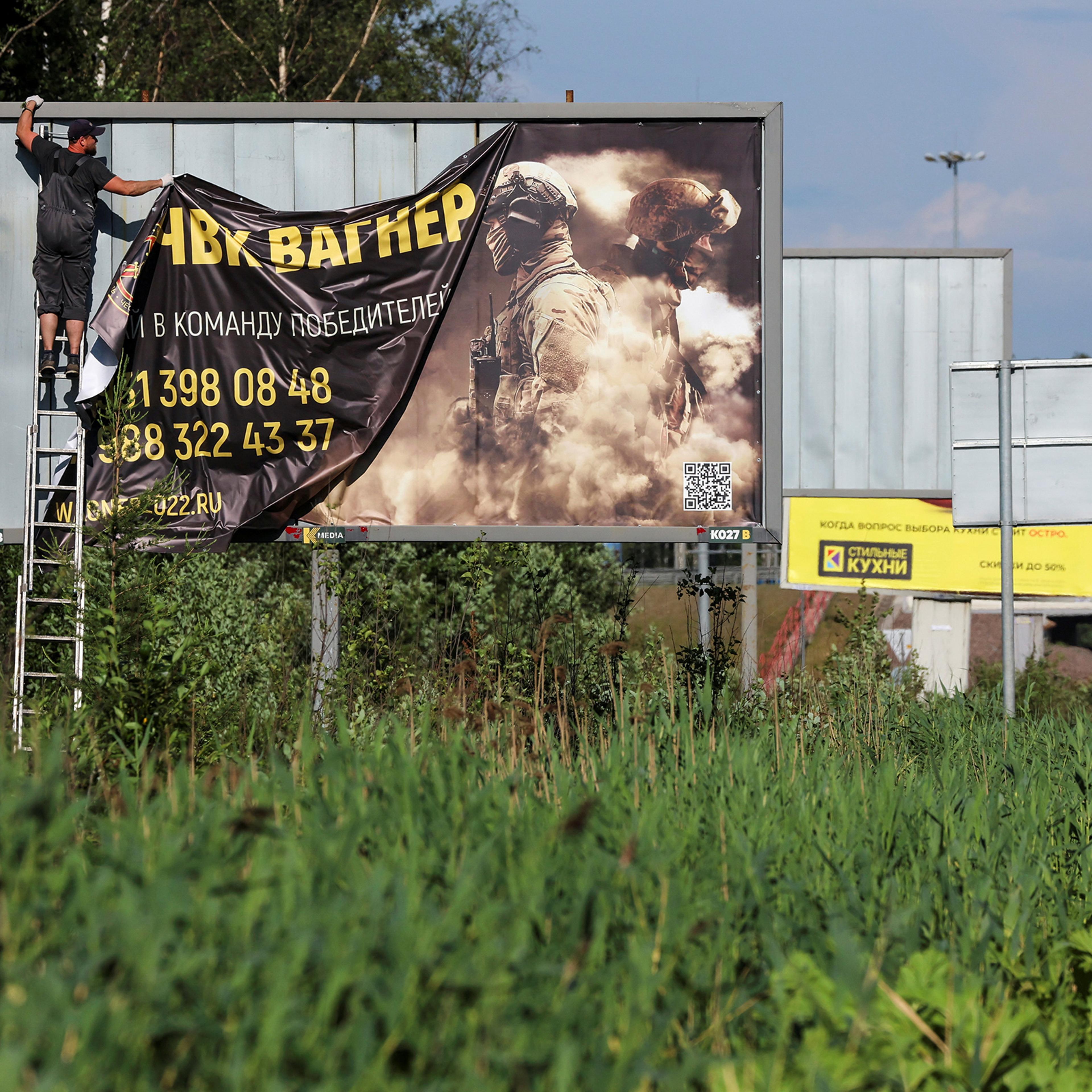 A worker removes an advertising banner promoting service in Wagner private mercenary group on the outskirts of Saint Petersburg, Russia, on June 24. A slogan on the banner reads: "Accede to the team of victors!"