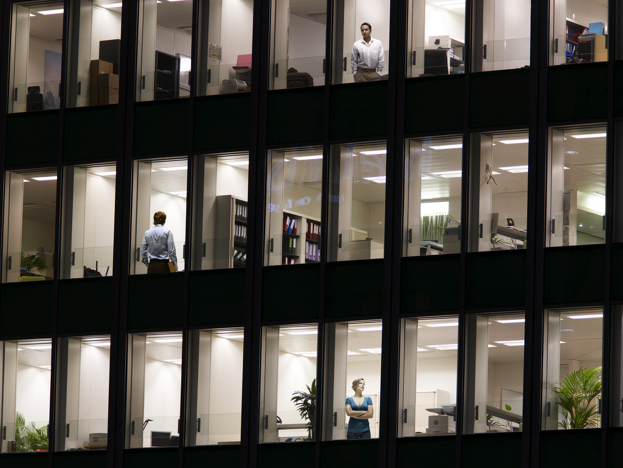 Illuminated office building with workers at window, night