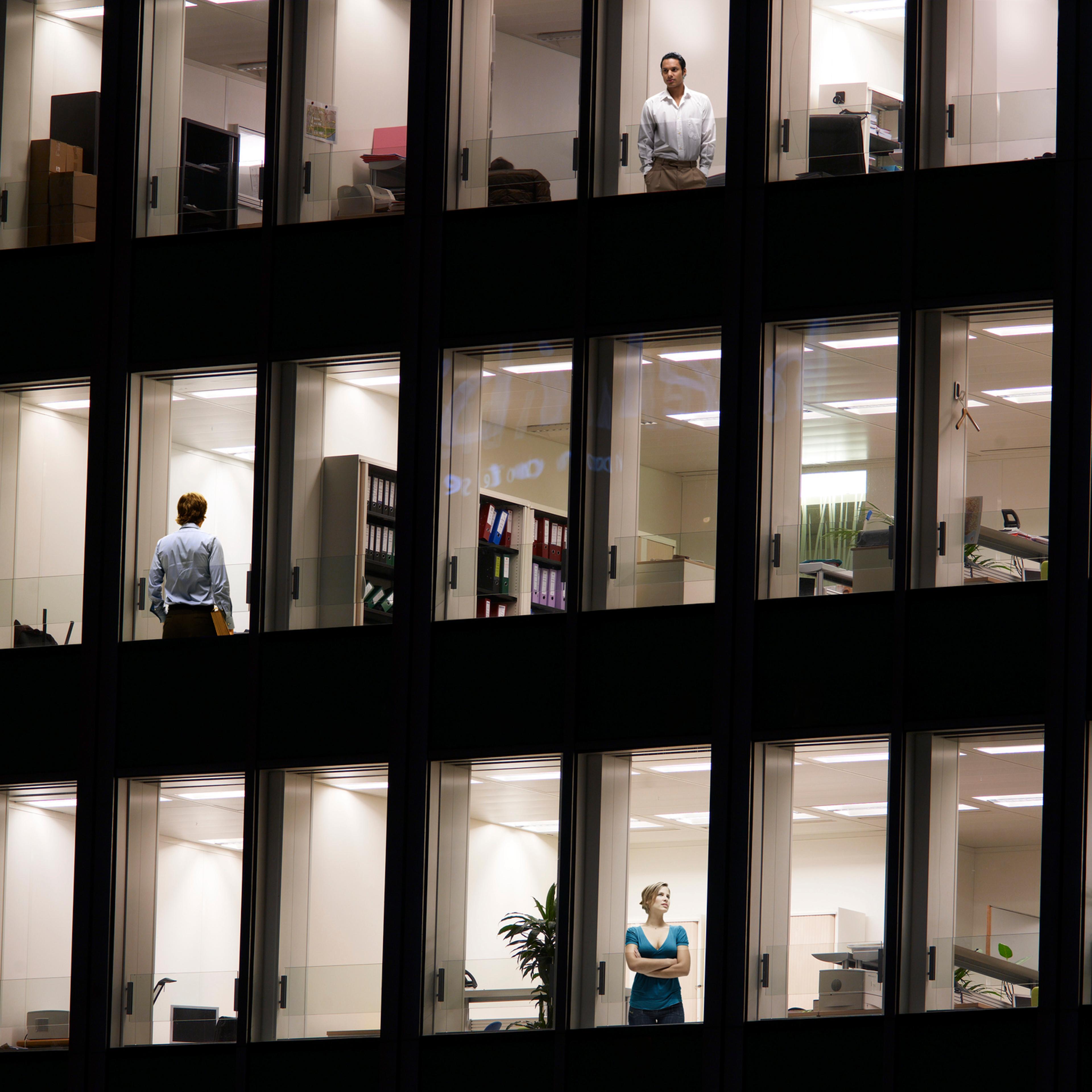 Illuminated office building with workers at window, night