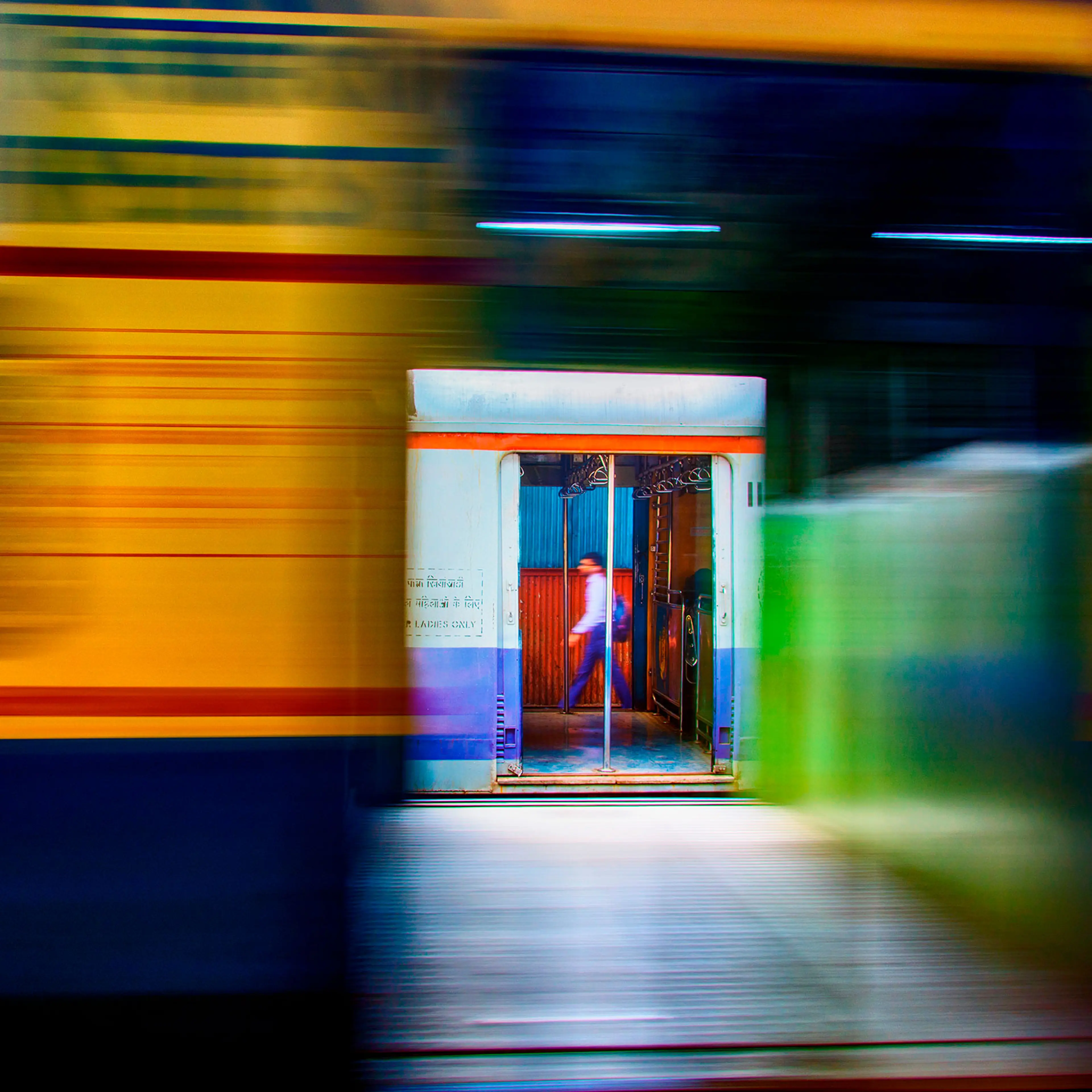 A daily commuter in blurred motion walks on the platform while another local train passes by in Mumbai