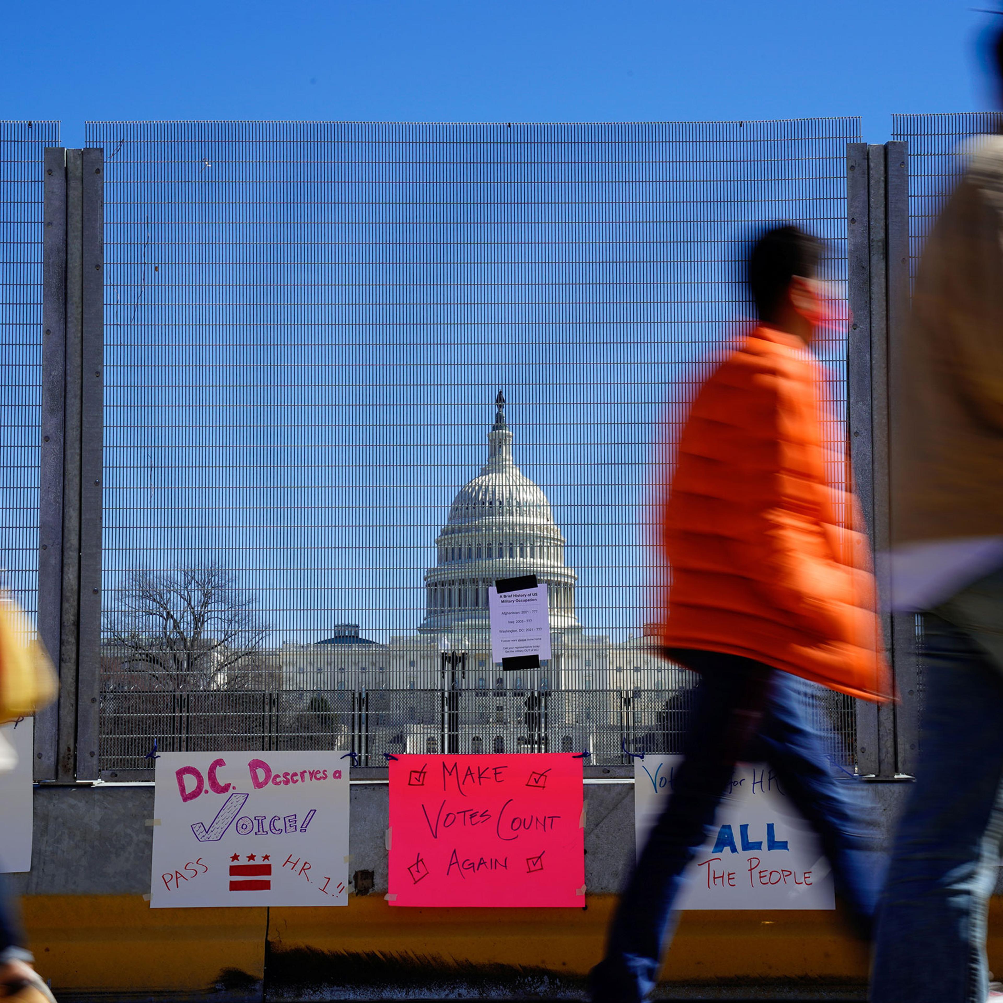 People walk past signs hung on a security fence in support of expanded voting rights near the U.S. Capitol in Washington
