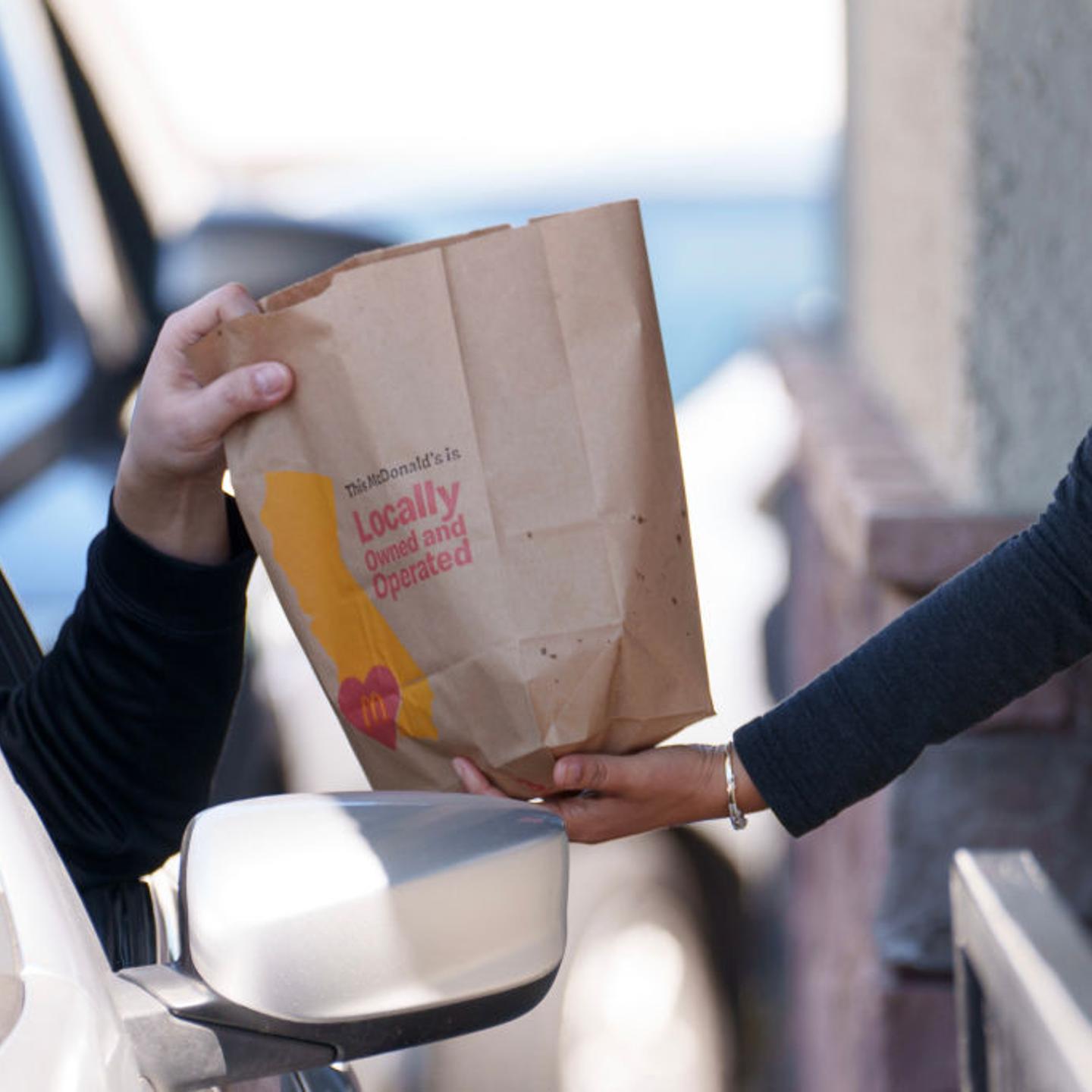 An employee hands a bag to a customer at the drive-thru
