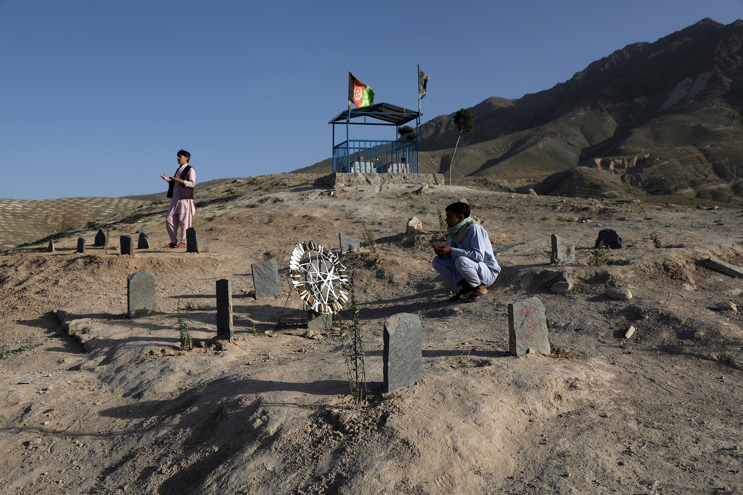 Afghan men pray near the grave of relatives, who were killed in the May bombings near Syed Al-Shahada girls school, at a cemetery on the outskirts of Kabul on June 2, 2021.