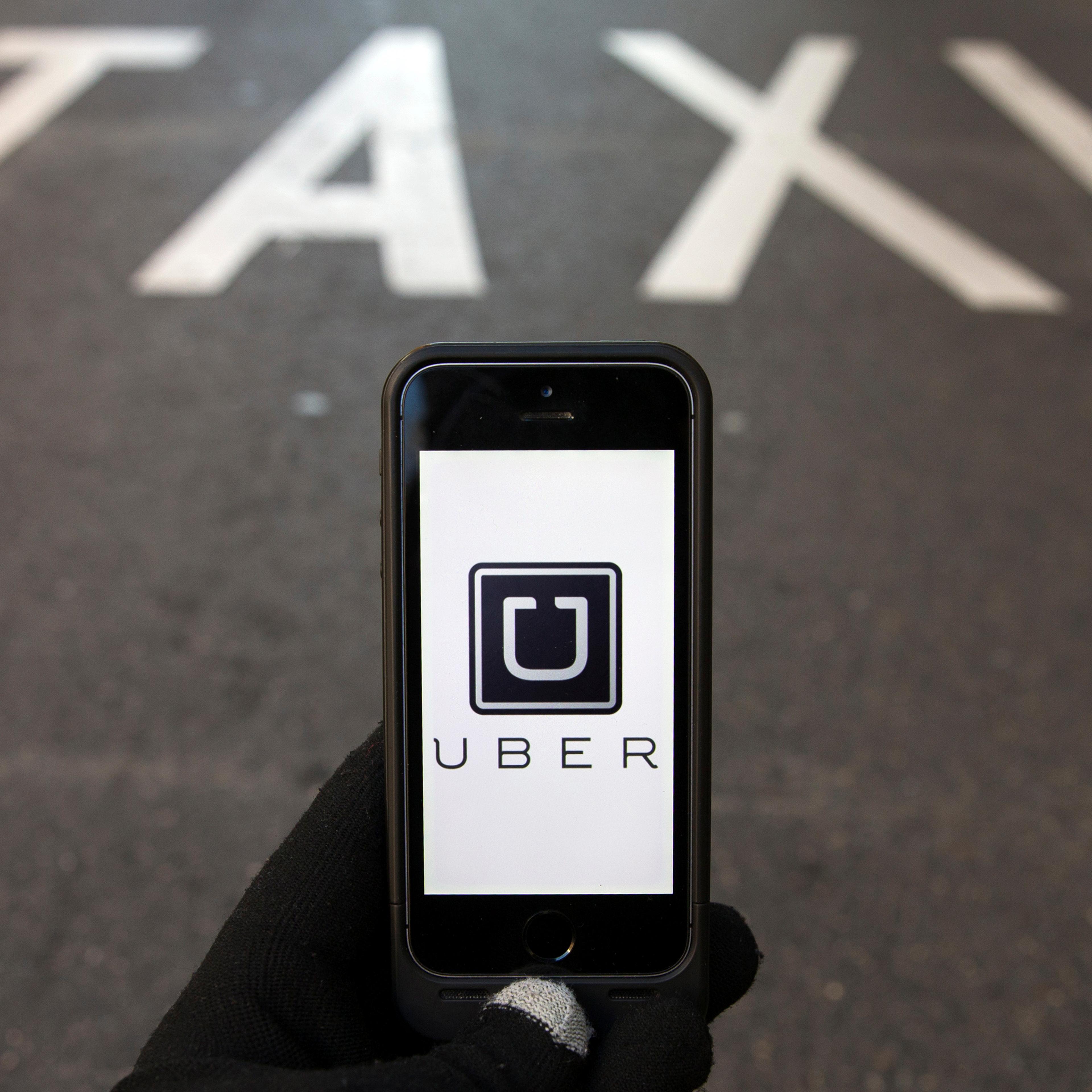 Photo illustration of logo of car-sharing service app Uber on a smartphone over a reserved lane for taxis in a street in Madrid
