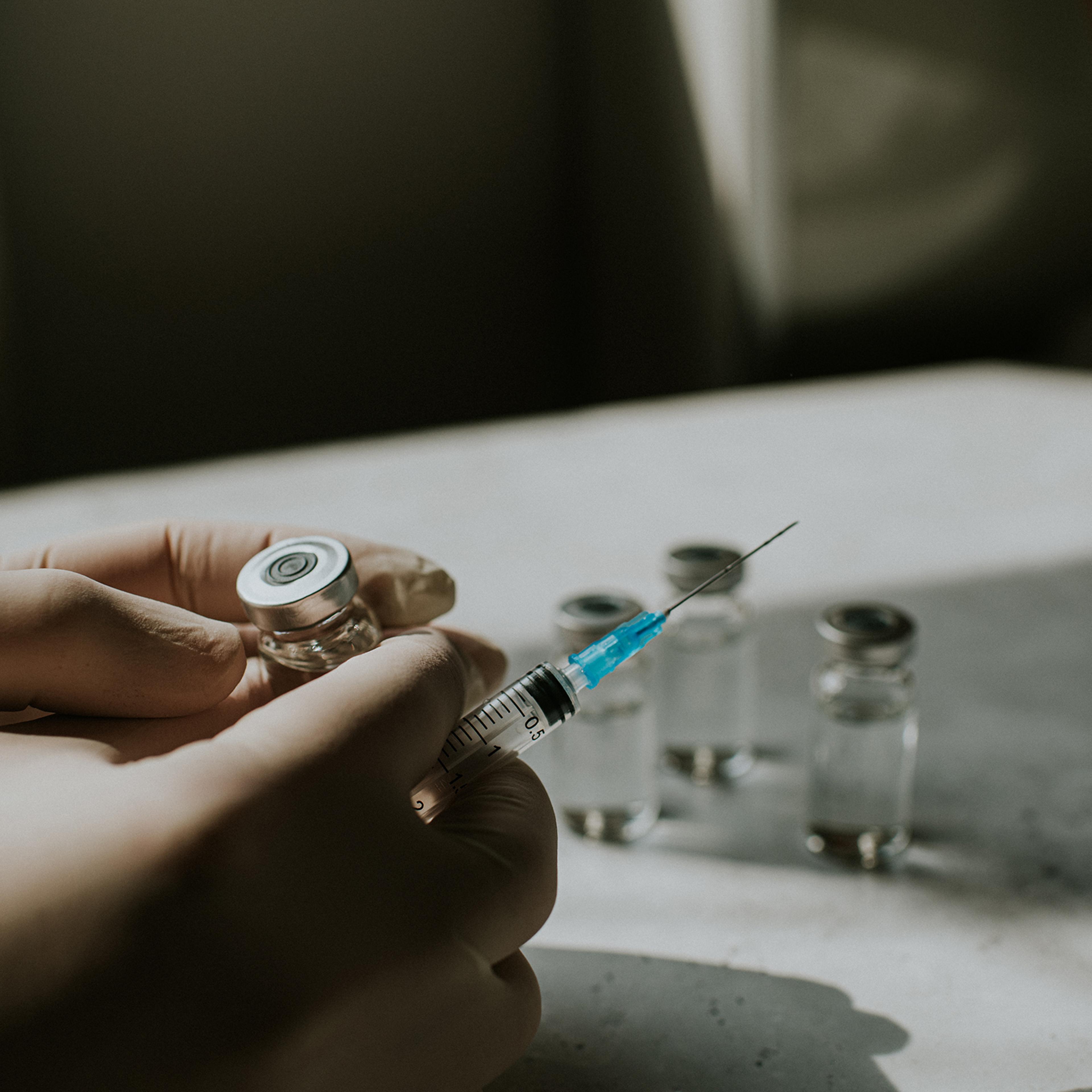 Gloved hand holds a syringe and a vial