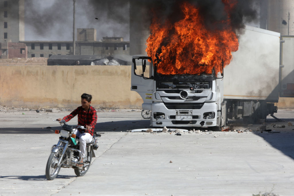 A man rides a motorcycle near a burning Turkish truck during protests against Turkey in al-Bab, Syria.