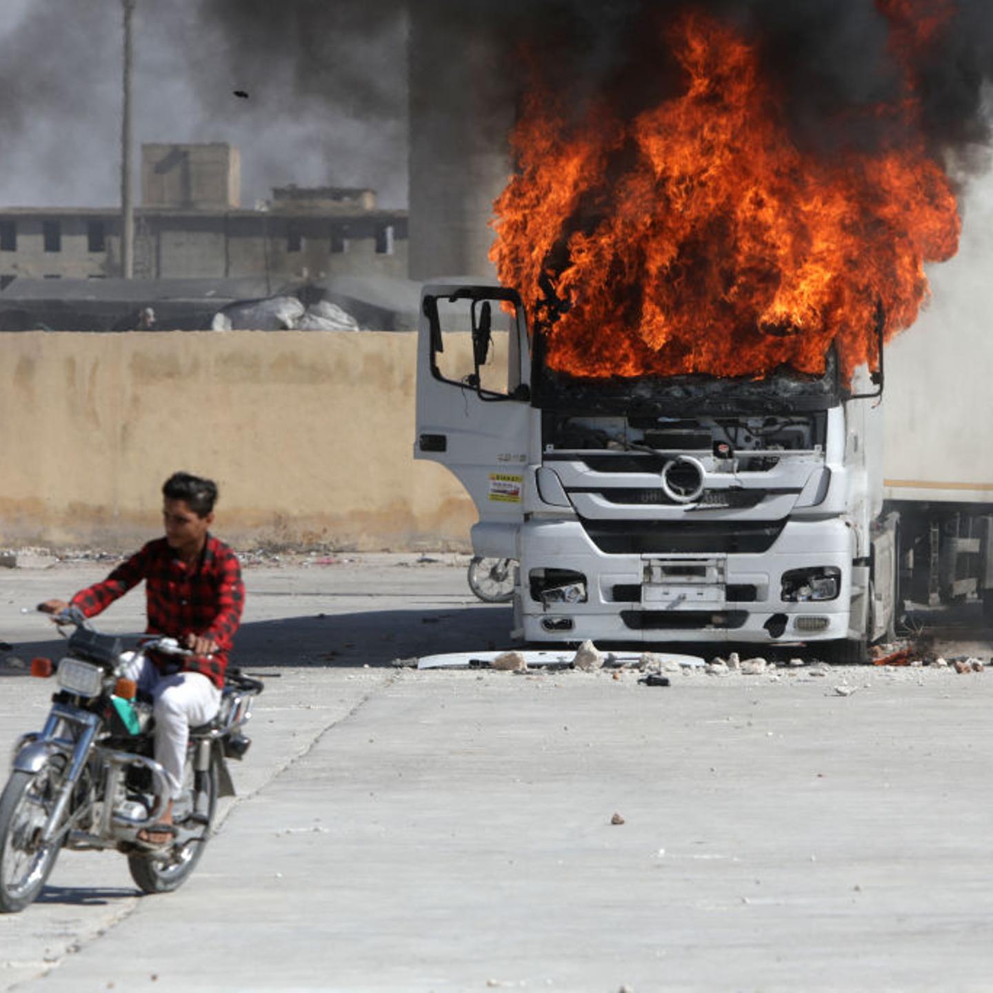 A man rides a motorcycle near a burning Turkish truck during protests against Turkey in al-Bab, Syria.