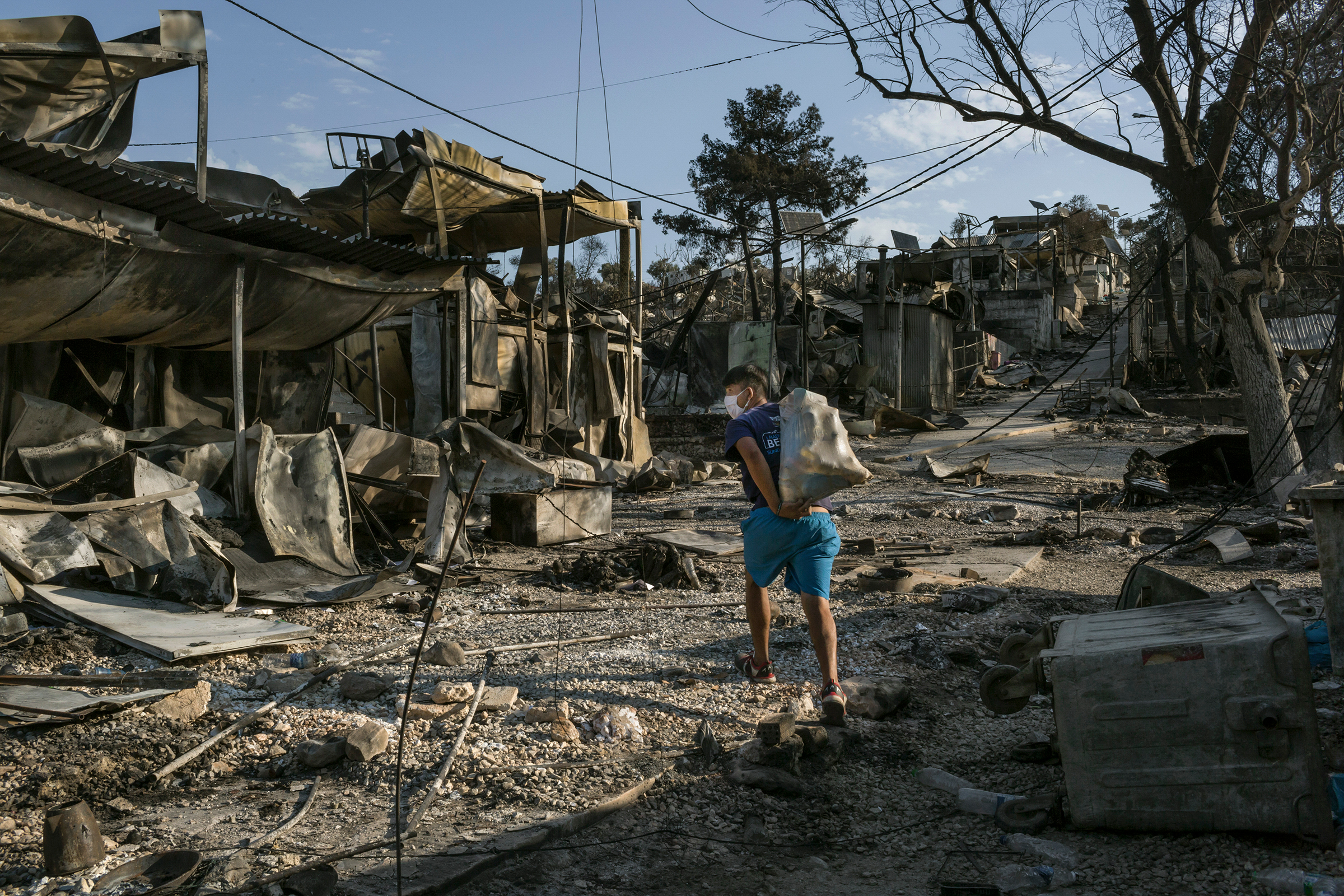 A migrant from Afghanistan carries some of his belongings through the destroyed Moria camp on Lesbos, Greece, on Sept. 12, 2020. The camp, already a bleak emblem of Europe's migrant policy, was locked down after a coronavirus outbreak, prompting some asy