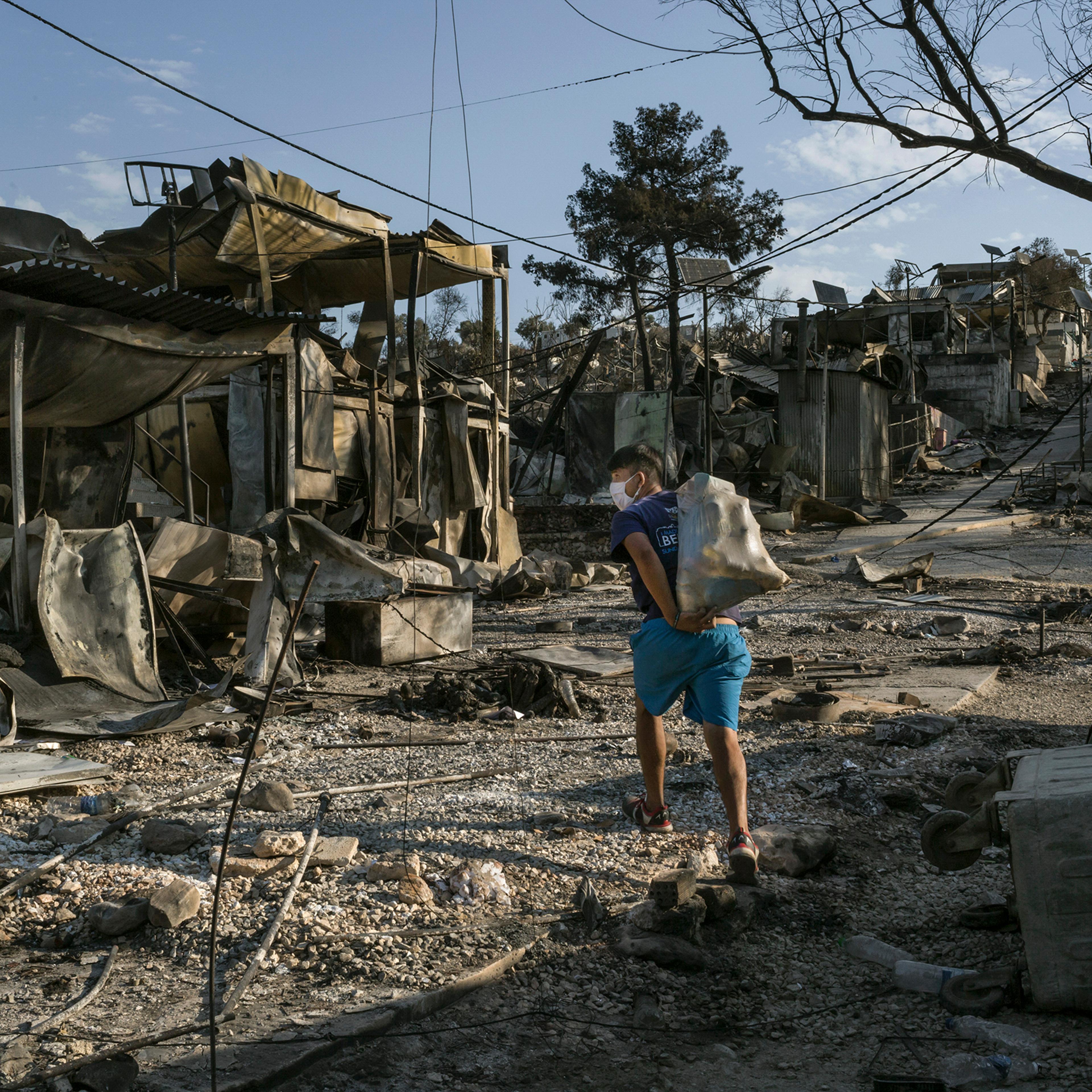 A migrant from Afghanistan carries some of his belongings through the destroyed Moria camp on Lesbos, Greece, on Sept. 12, 2020. The camp, already a bleak emblem of Europe's migrant policy, was locked down after a coronavirus outbreak, prompting some asy