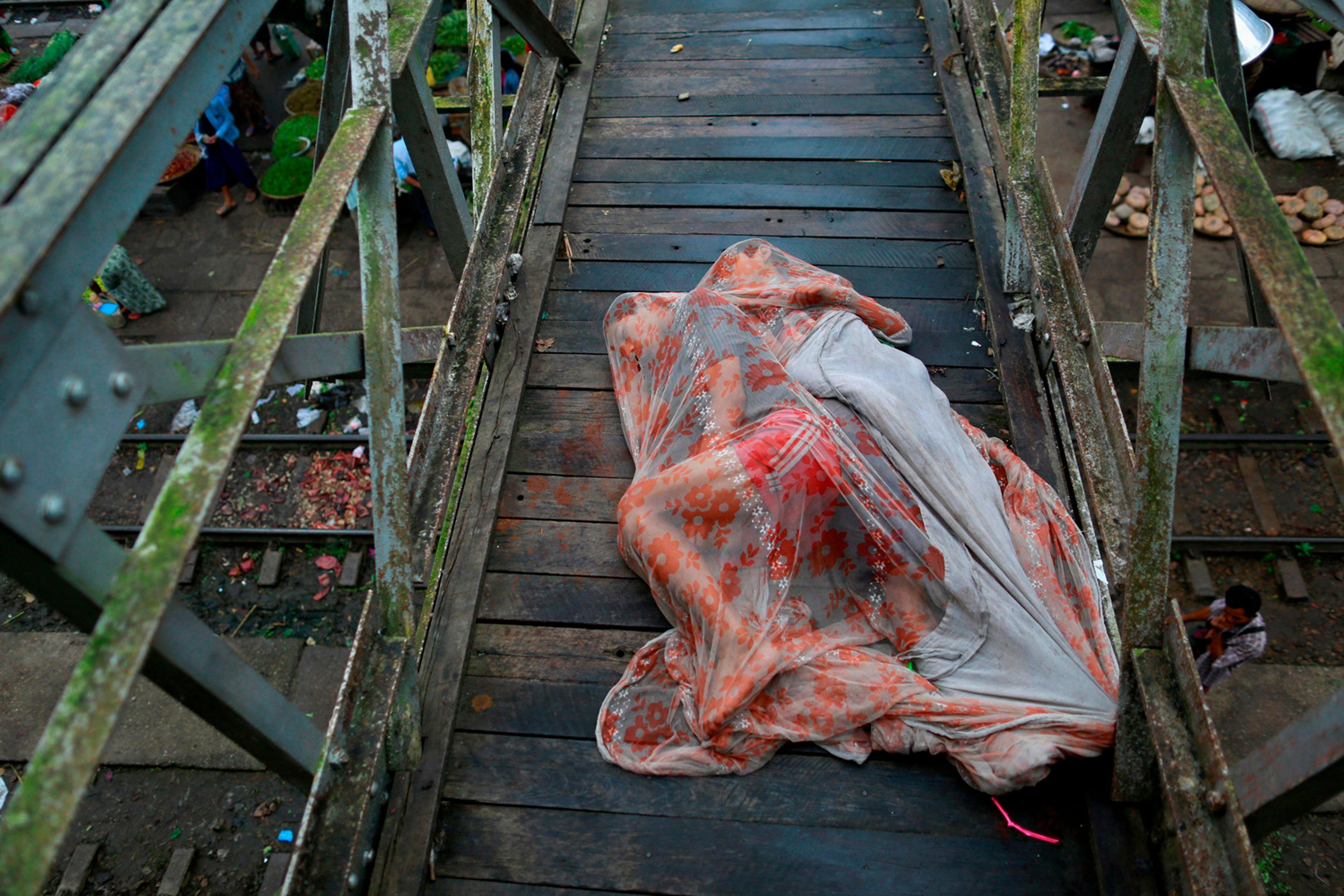 Men sleep covered with a mosquito net on a bridge above a train station outside Yangon