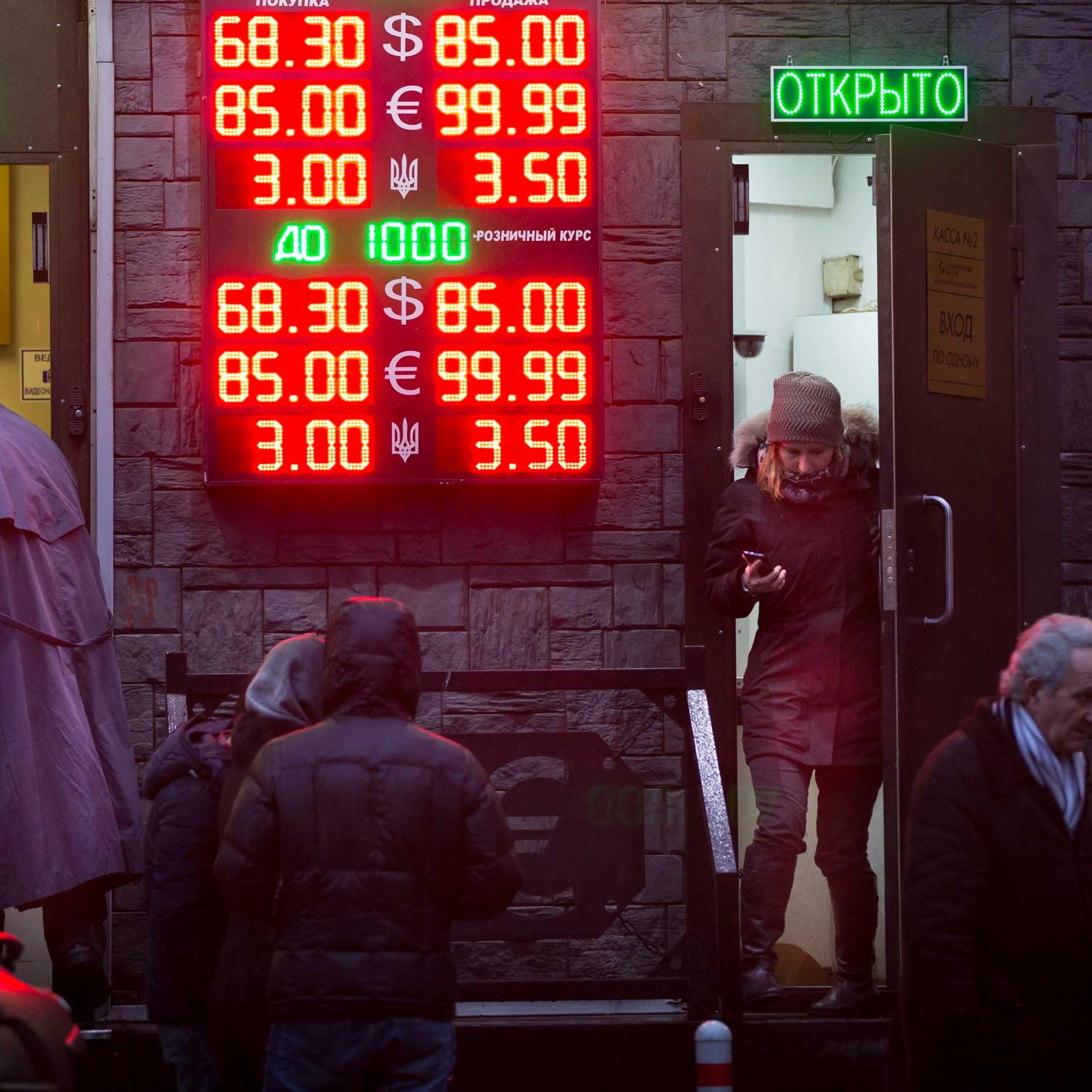 People wait to exchange their currency as signs advertise the exchange rates at a currency exchange office in Moscow, Dec. 16, 2014.