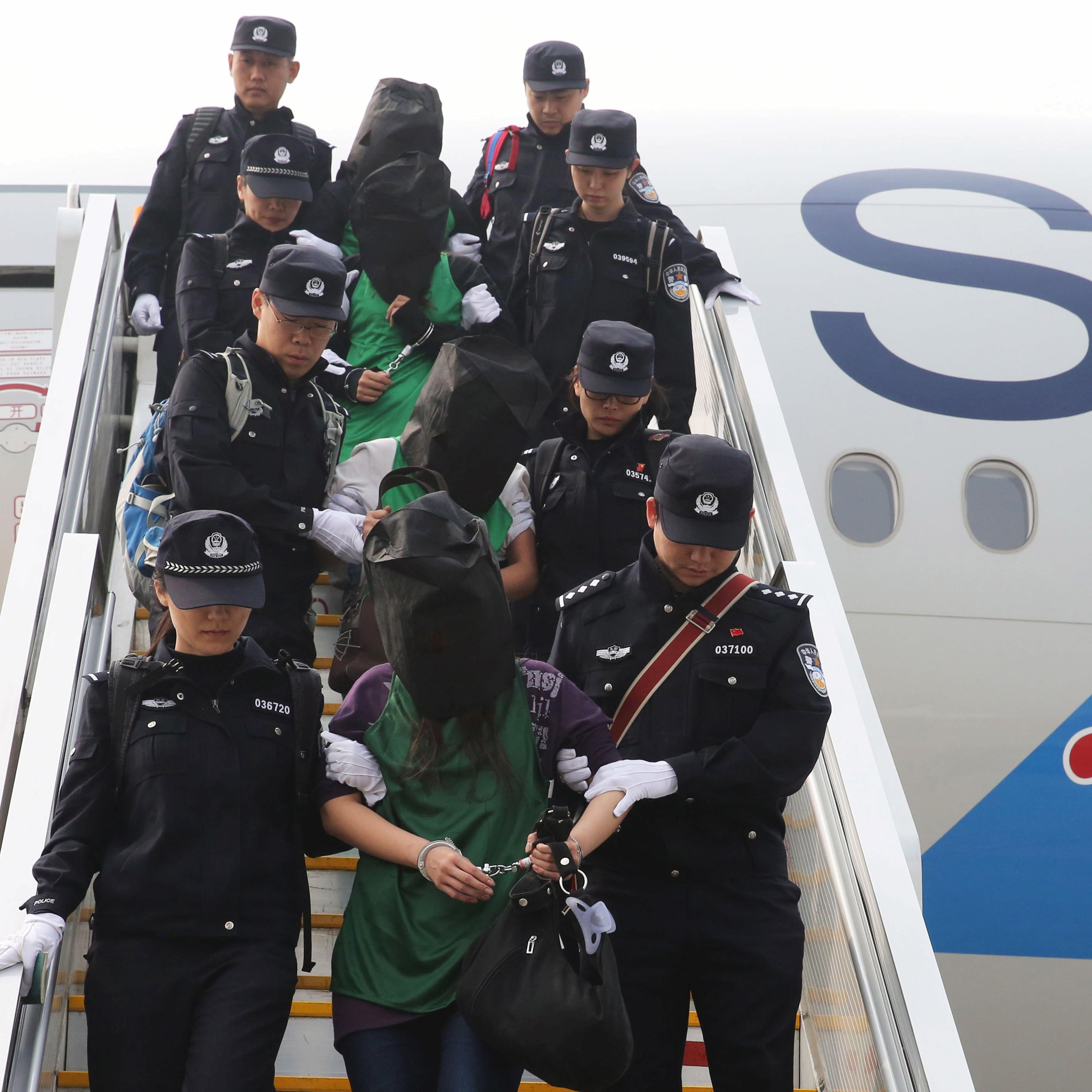 Police escort a group of people wanted for suspected fraud in China, after they were deported from Kenya, as they get off a plane after arriving at Beijing Capital International Airport in Beijing