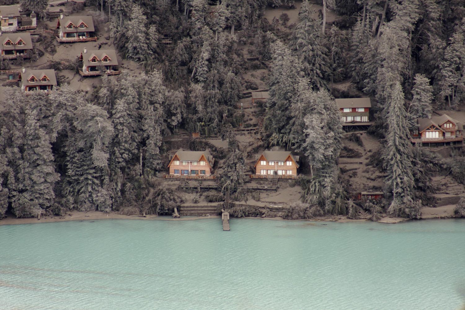 Houses and trees are covered by volcanic ash on the bank of Nahuel Huapi Lake in Villa La Angostura in southern Argentina, Sunday June 19, 2011. The Chilean government says the volcano in southern Chile that began erupting about two weeks ago is becoming less active. That will allow 4,000 people who were evacuated near the volcano to return home.