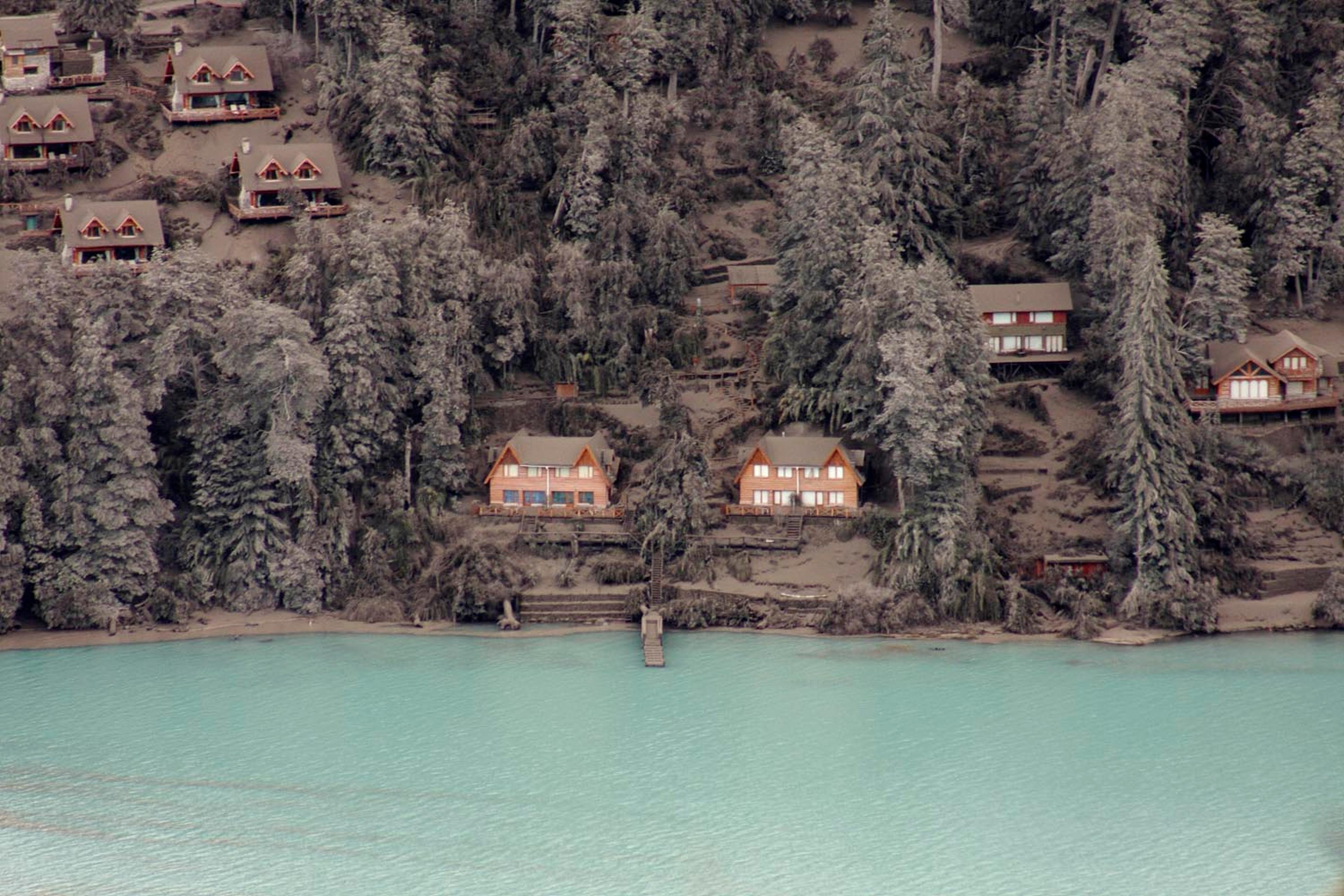 Houses and trees are covered by volcanic ash on the bank of Nahuel Huapi Lake in Villa La Angostura in southern Argentina, Sunday June 19, 2011. The Chilean government says the volcano in southern Chile that began erupting about two weeks ago is becoming less active. That will allow 4,000 people who were evacuated near the volcano to return home.
