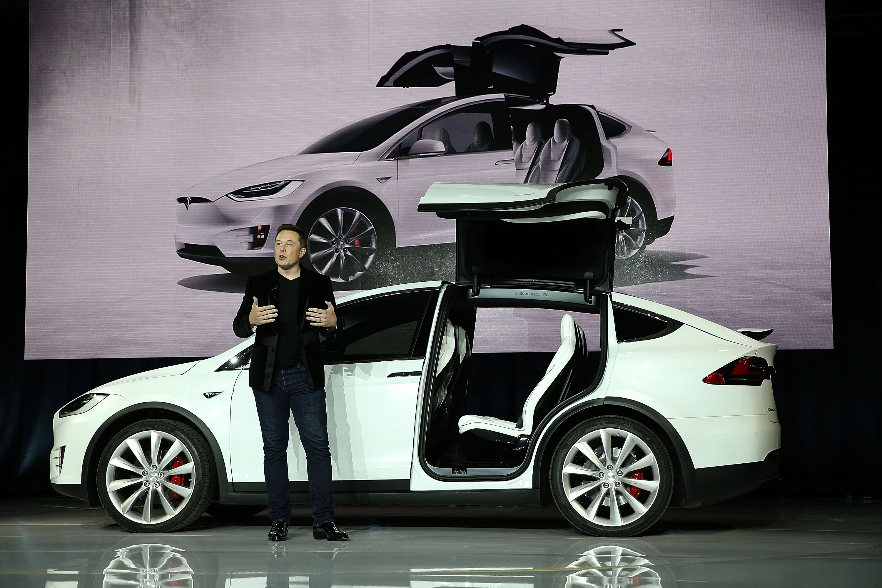 Elon Musk in front of a white Tesla vehicle
