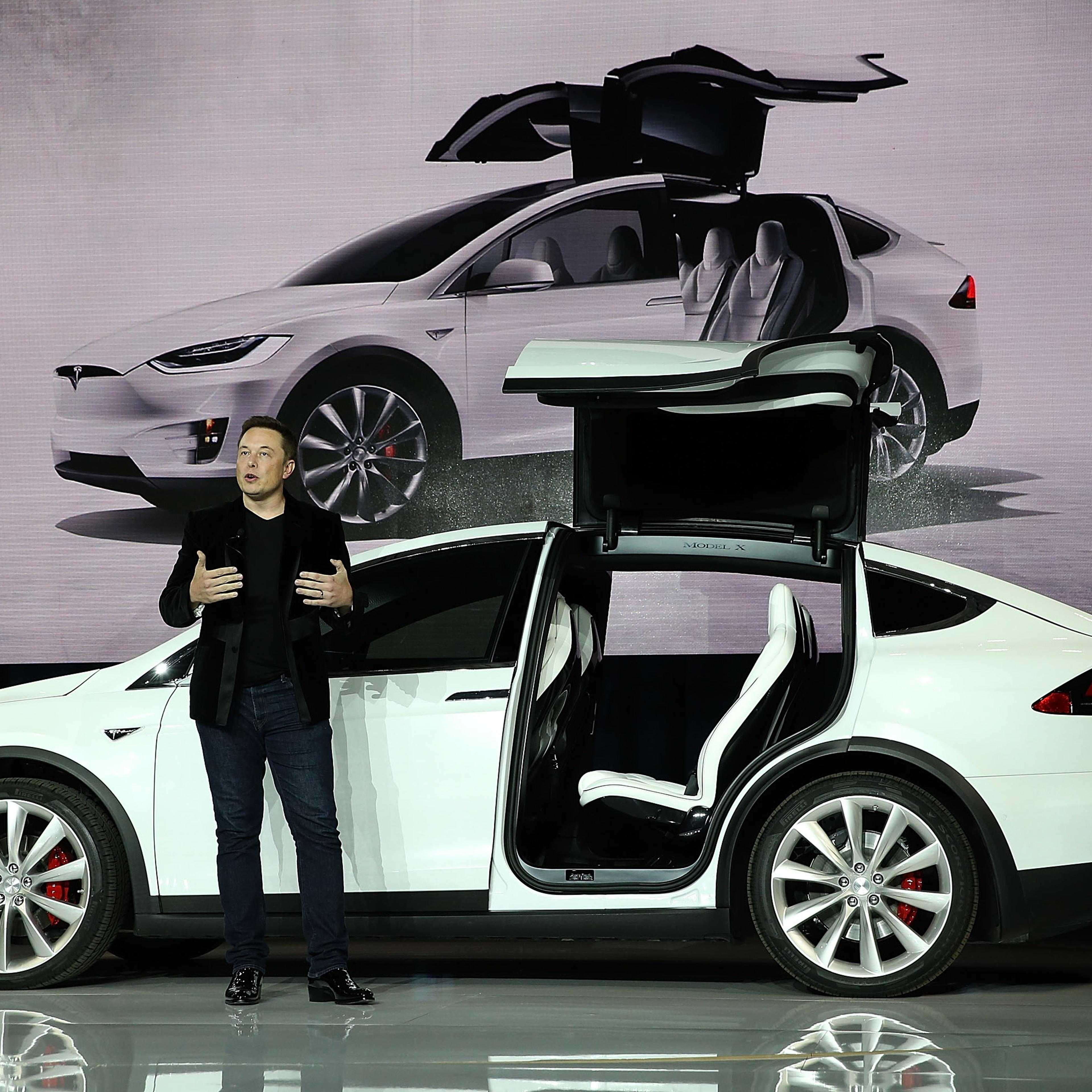 Elon Musk in front of a white Tesla vehicle