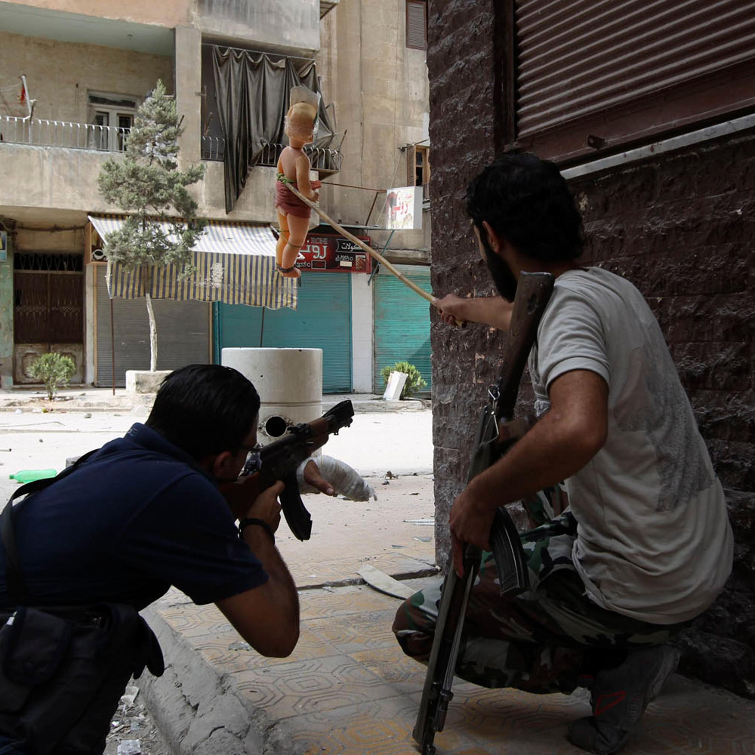 A Kurdish Free Syrian Army fighter holds doll while his fellow fighter takes shooting position in Ashrafieh, Aleppo