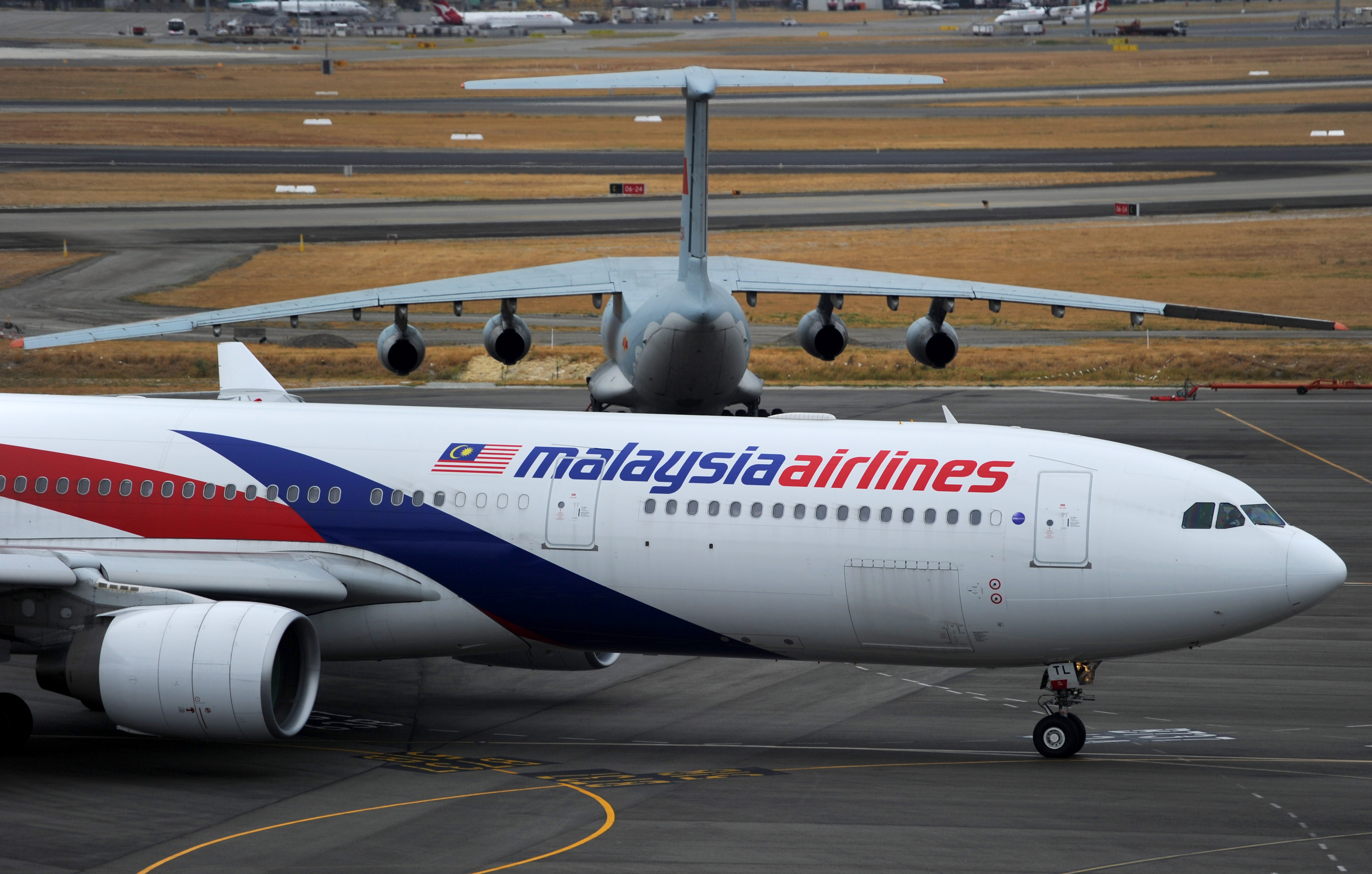A Malaysia Airlines plane prepares to go out onto the runway and passes by a stationary Chinese Ilyushin 76 aircraft (top) at Perth International Airport on March 25, 2014 in Perth, Australia.