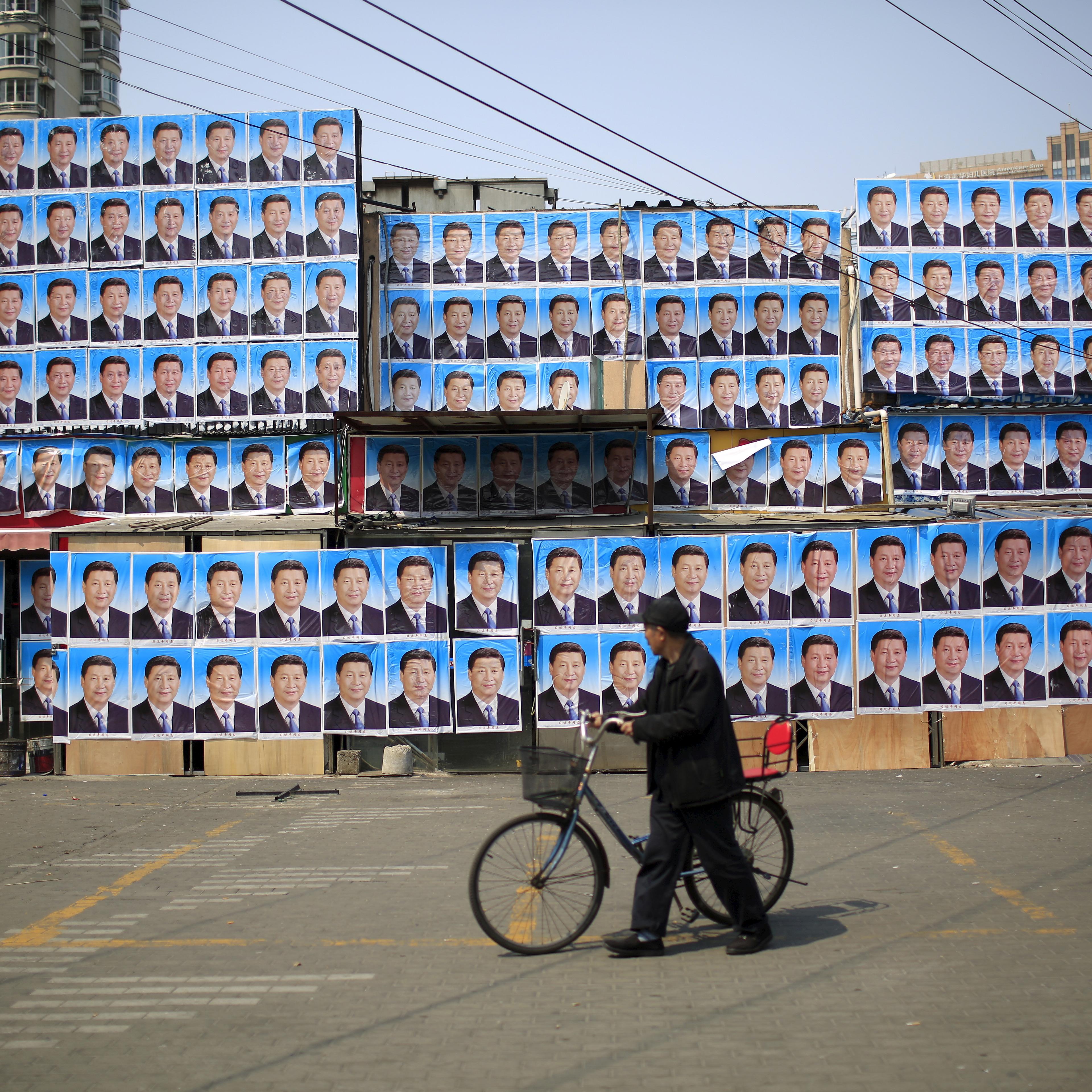 A man with a bicycle walks past a building covered in posters of Chinese President Xi Jinping in Shanghai