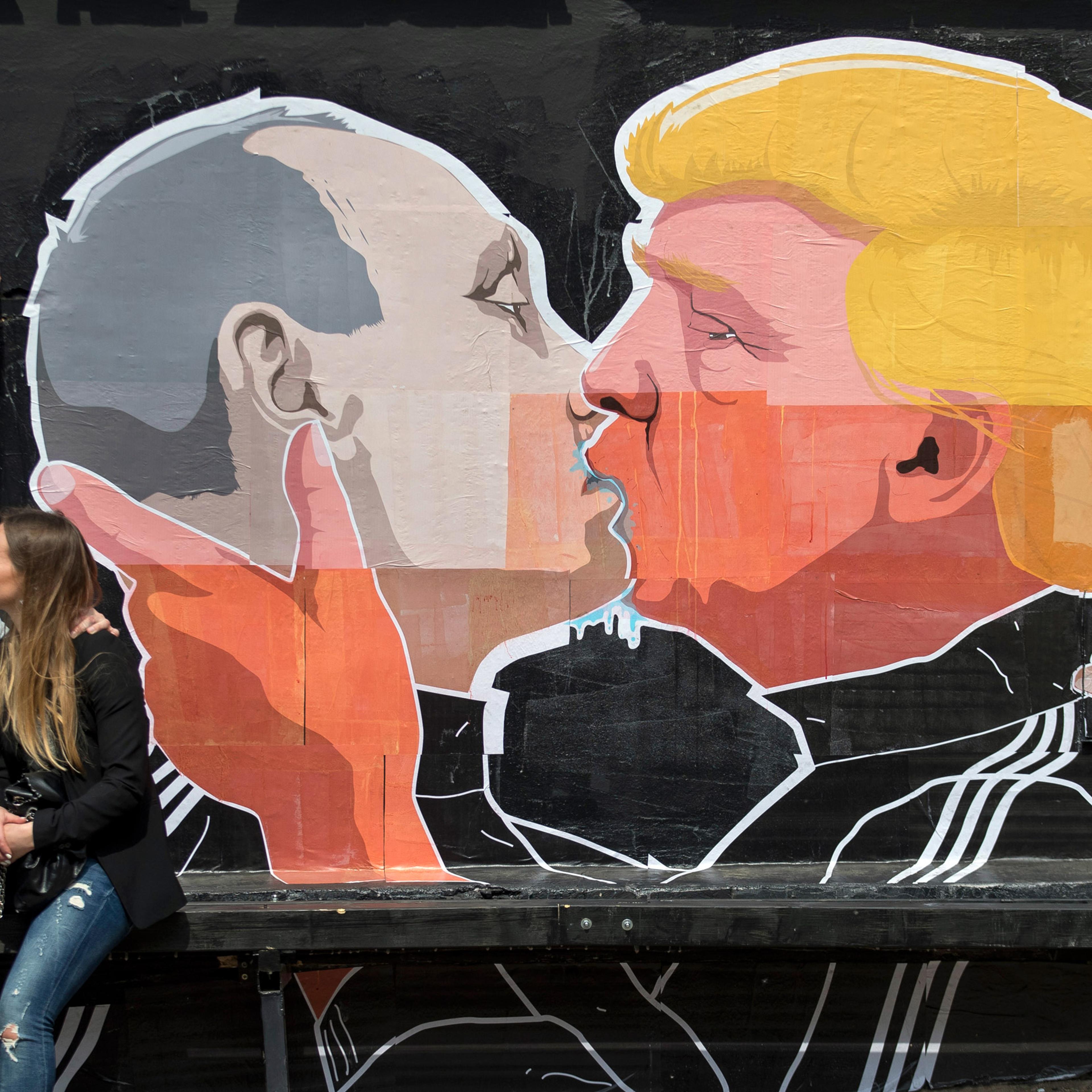 A couple kisses in front of graffiti depicting Russian President Vladimir Putin, left, and Republican presidential candidate Donald Trump, on the walls of a bar in the old town in Vilnius, Lithuania, Saturday, May 14, 2016. (AP Photo/Mindaugas Kulbis)