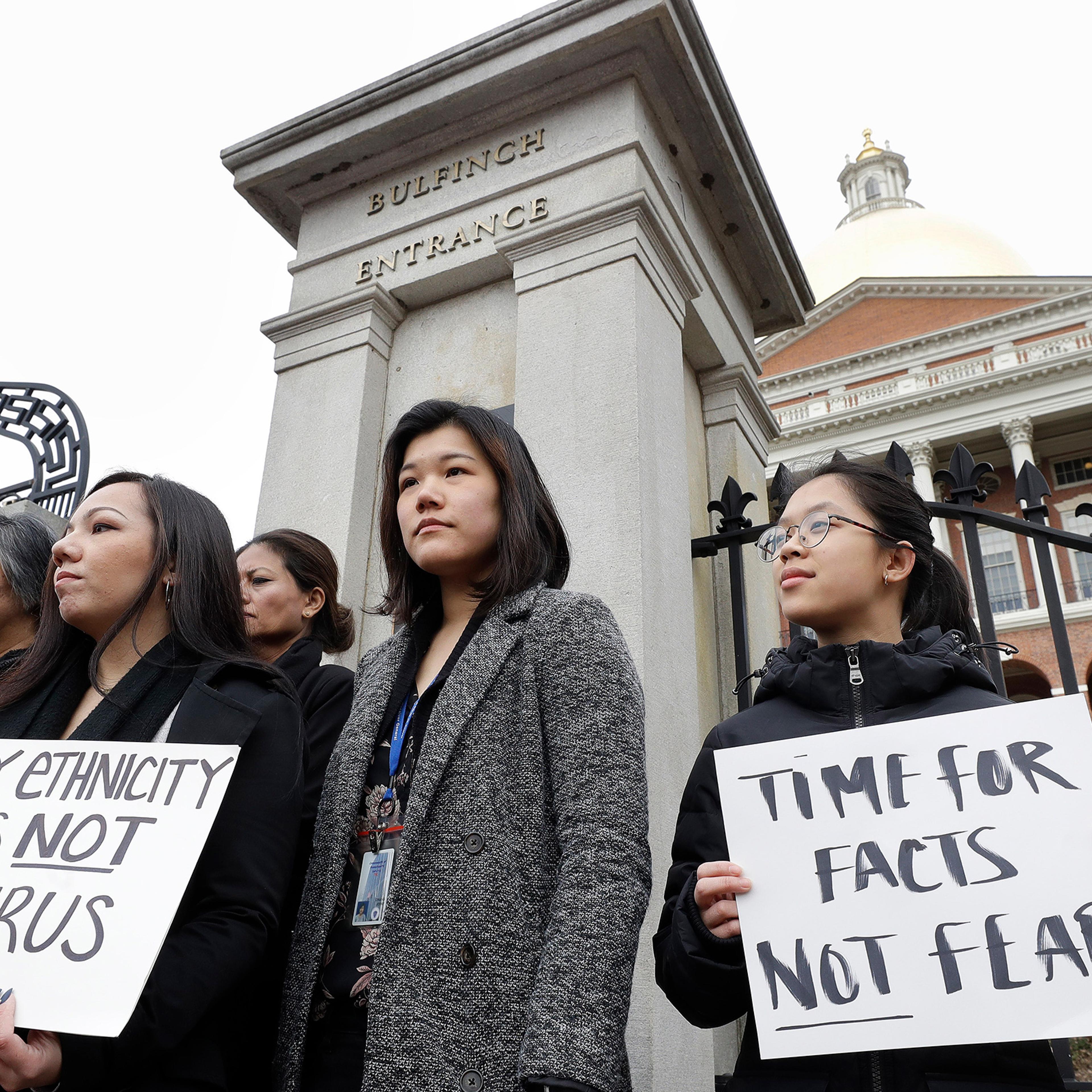 Jessica Wong, of Fall River, Mass., front left, Jenny Chiang, of Medford, Mass., center, and Sheila Vo, of Boston, from the state's Asian American Commission, stand together during a protest on March 12, 2020, on the steps of the Statehouse in Boston.