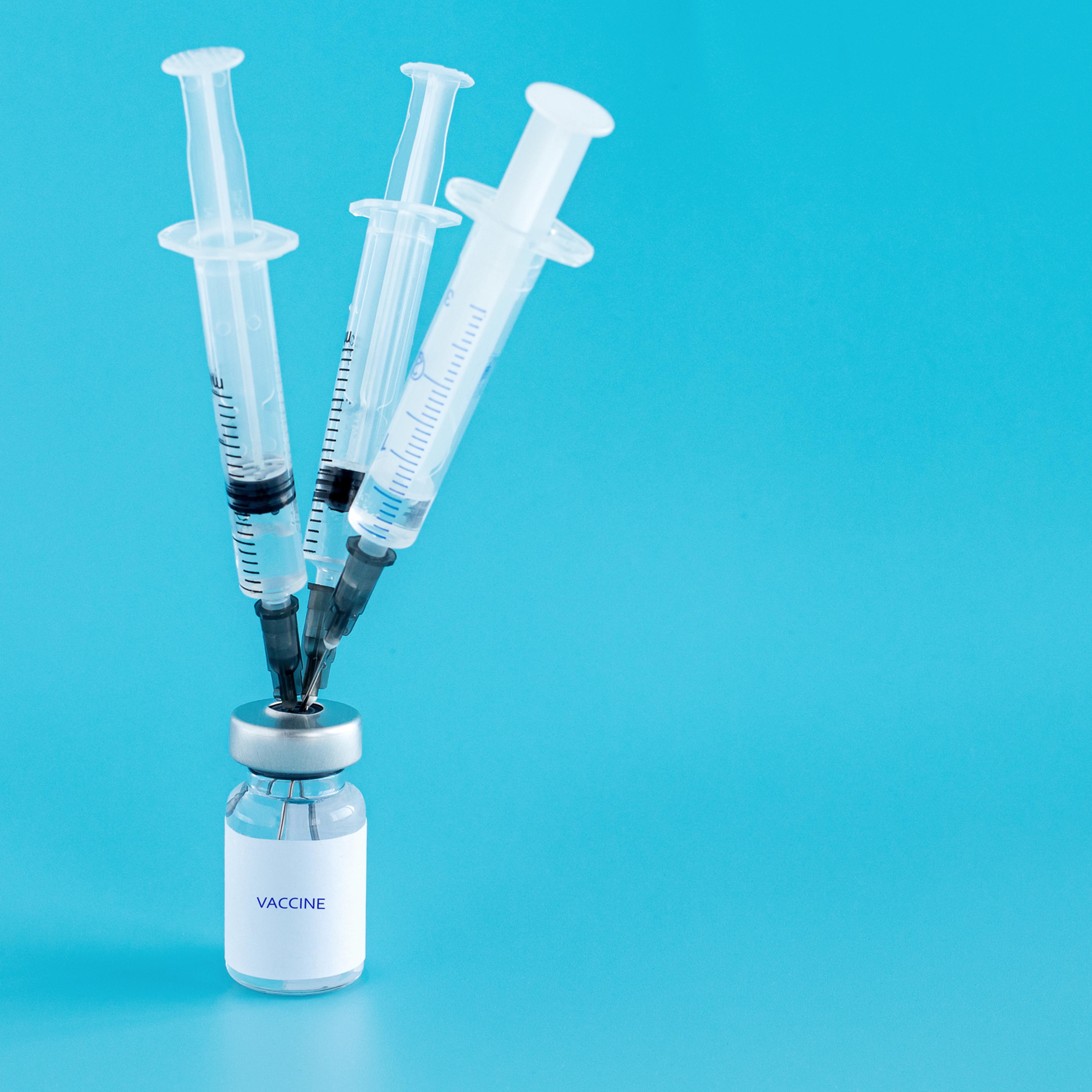 Bottle of vaccine, and three medical needles with injections stuck in the bottle cap on a blue isolated background. Vaccination against the flu, infections, covid-19. Copy space. Selective focus