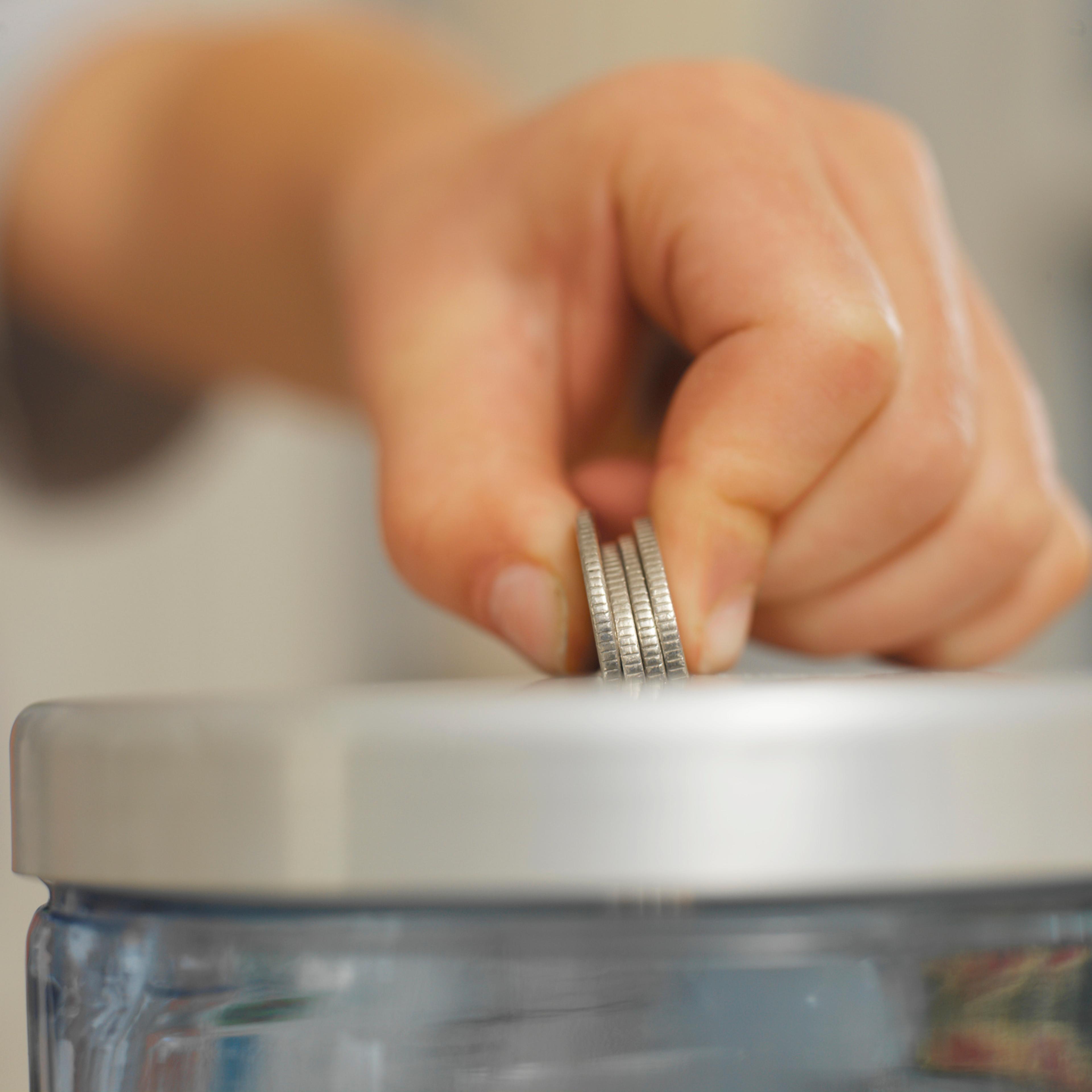 Boy placing coins in money jar, close-up