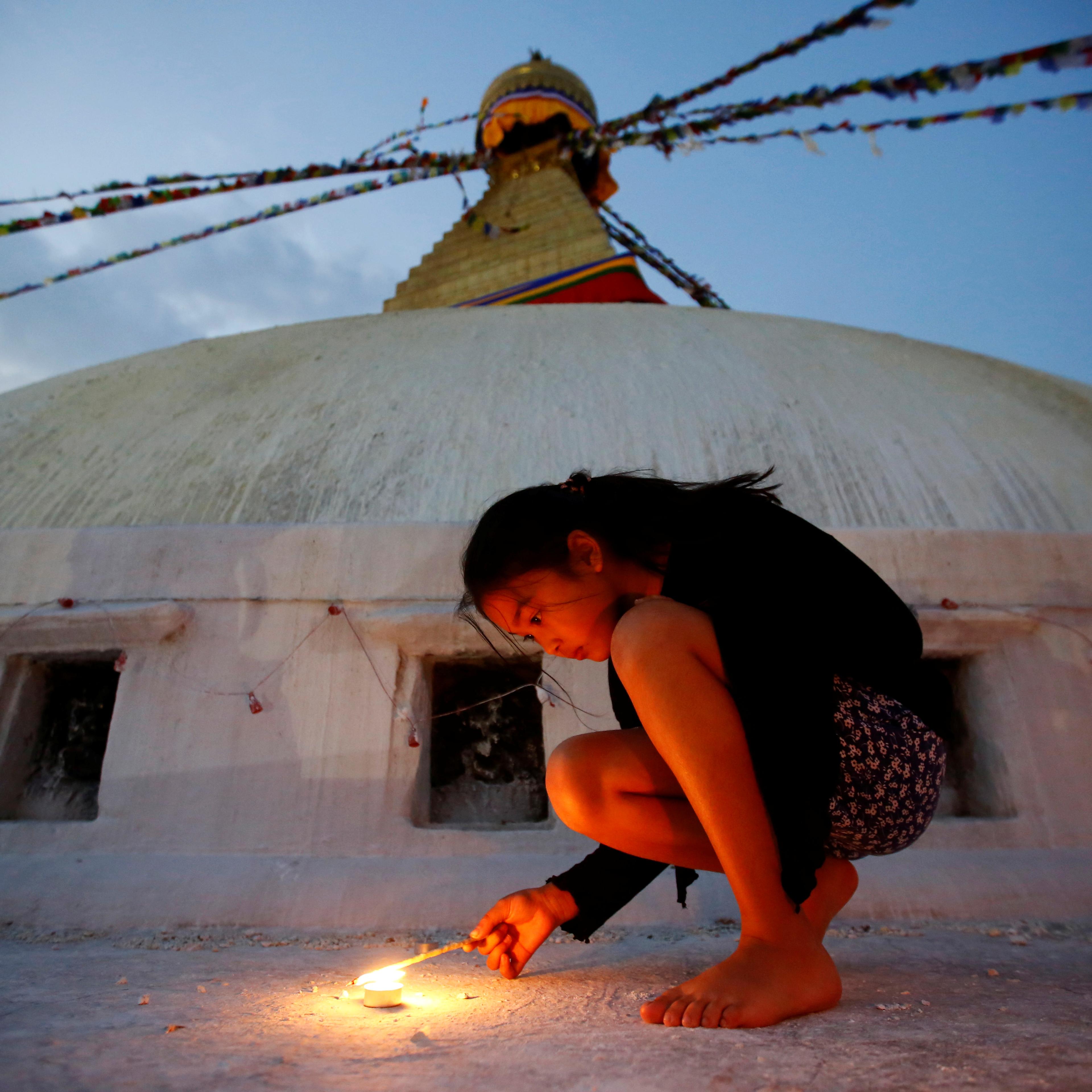 A girl lights a candle as she marks the anniversary of 2015 Nepal earthquake, at Boudhanath stupa in Kathmandu, Nepal