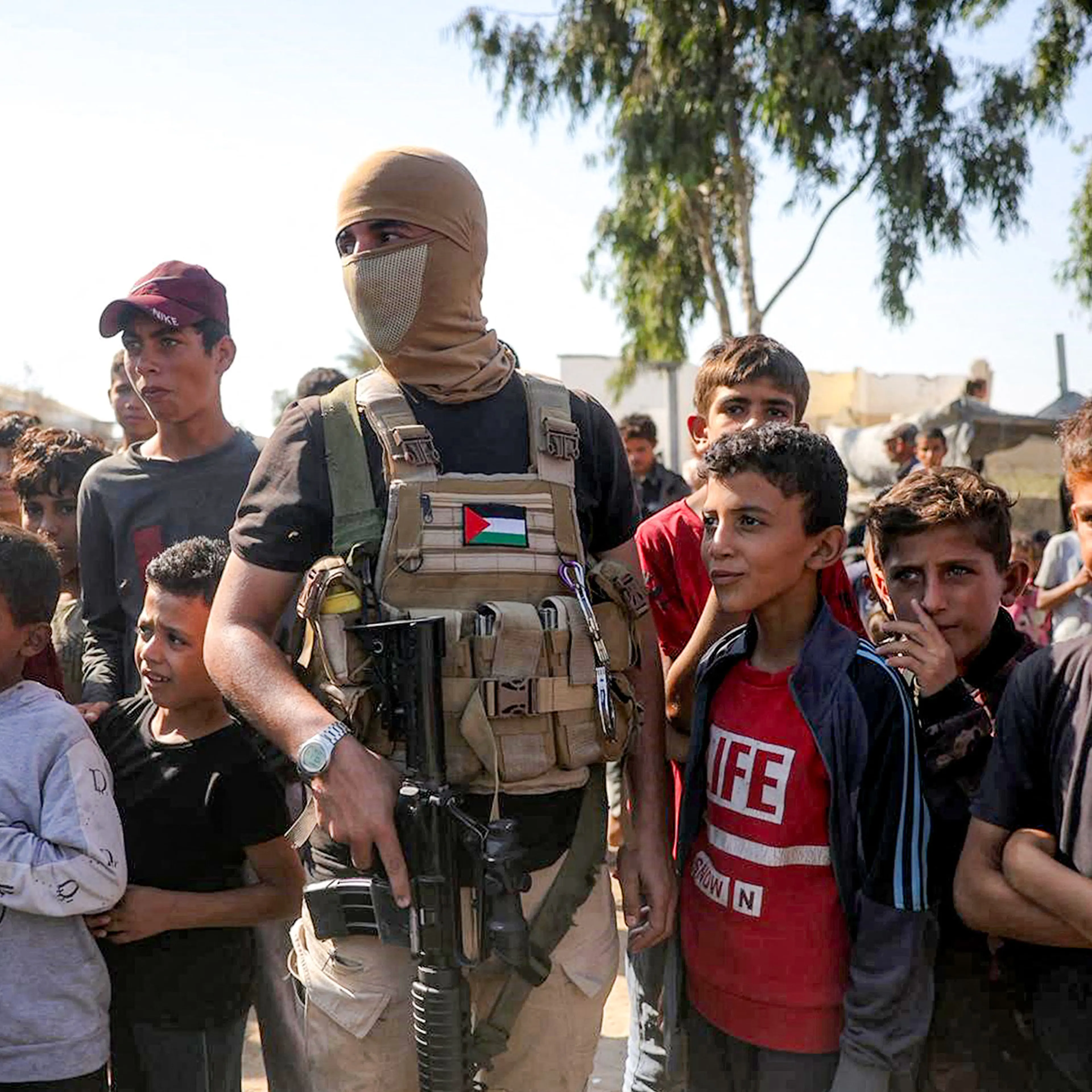 A masked Palestinian militant fighter of the Ezzedine al-Qassam Brigades, the armed wing of the Palestinian hamas movement, stands guard next to children before the arrival of vehicles of the International Committee of the Red Cross (ICRC) in the south o