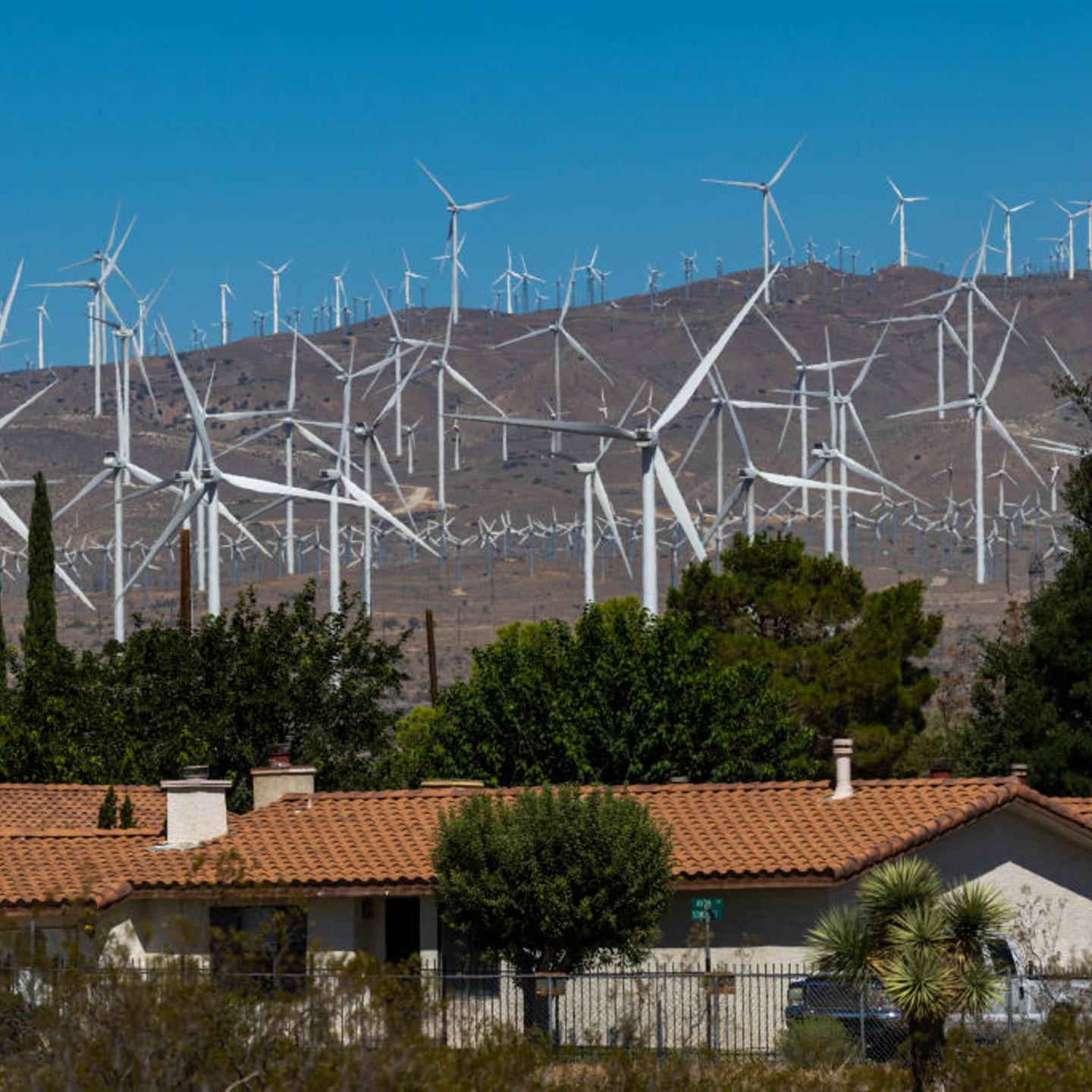 Wind turbines sprawl across the dessert next to a small community of homes.