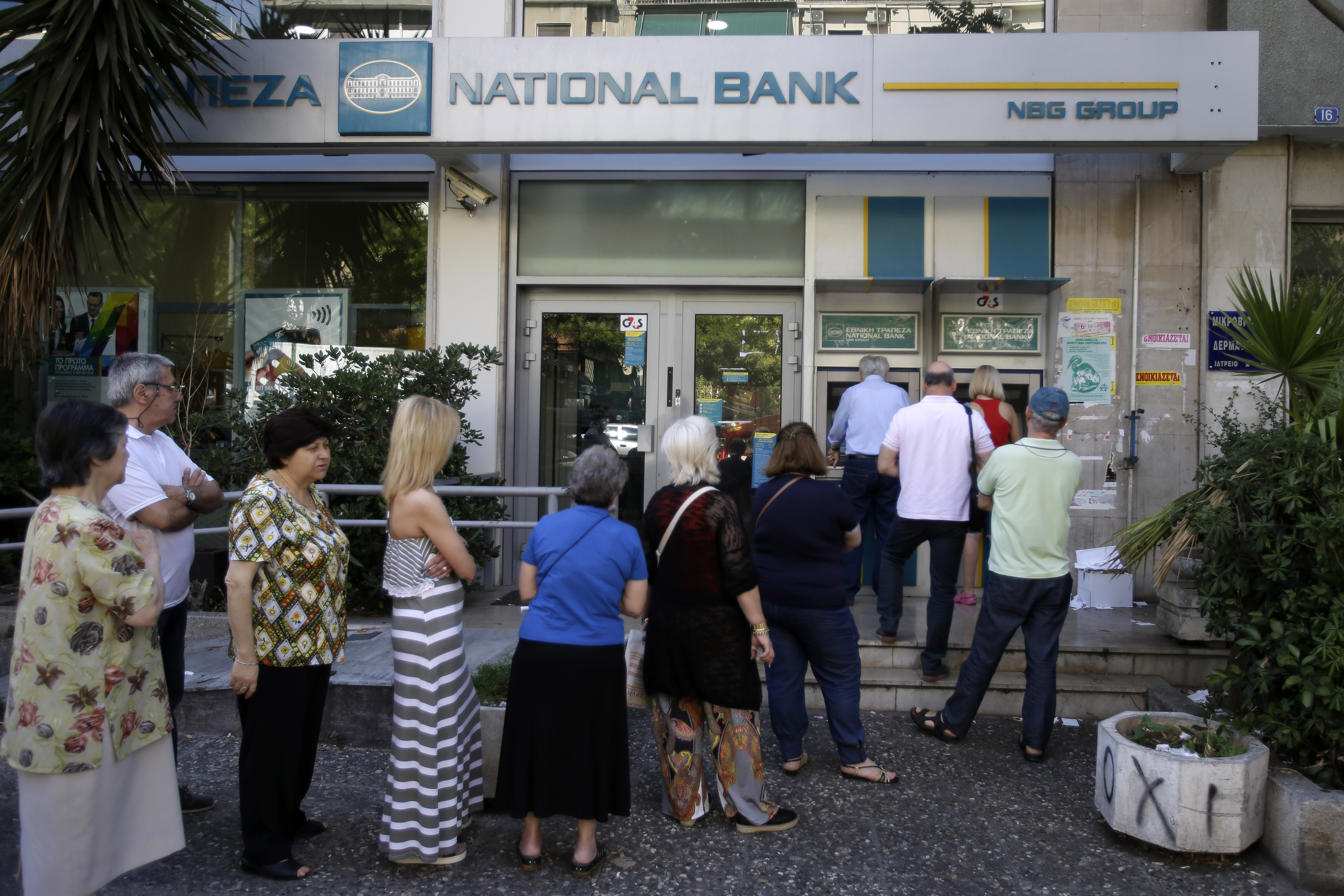 People stand in a queue to use an ATM outside a closed bank in Athens on June 30, 2015.