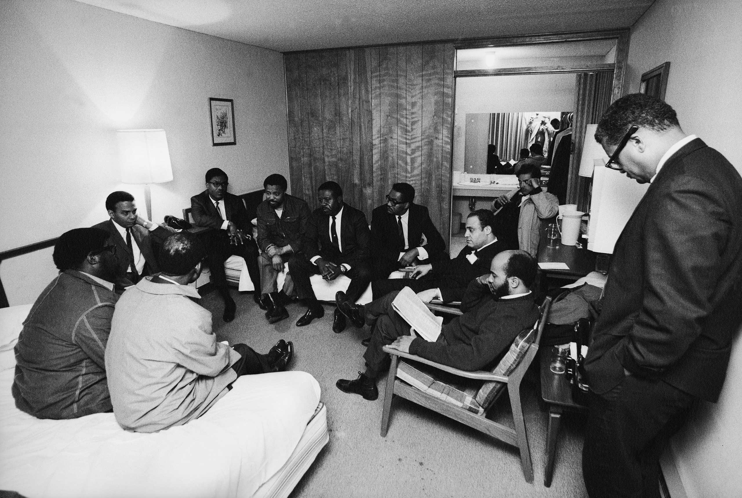 Stunned, silent members of the Southern Christian Leadership Conference in Dr. King's room at the Lorraine Motel, April 4, 1968, including Andrew Young (far left, under table lamp) and civil rights leader and Dr. King's colleague, Rev. Ralph Abernathy, i
