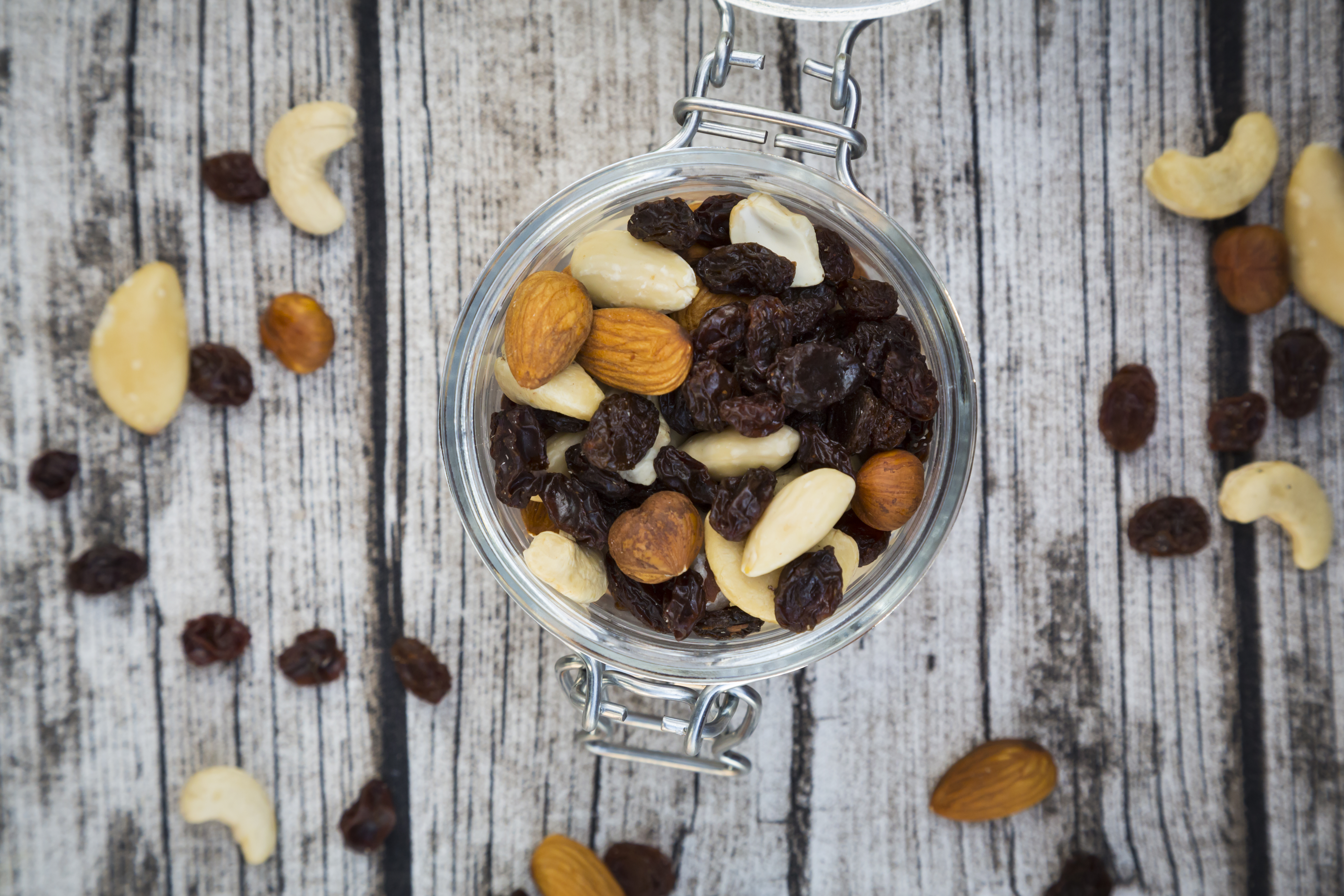 Mixed nuts and raisins in glass on wood