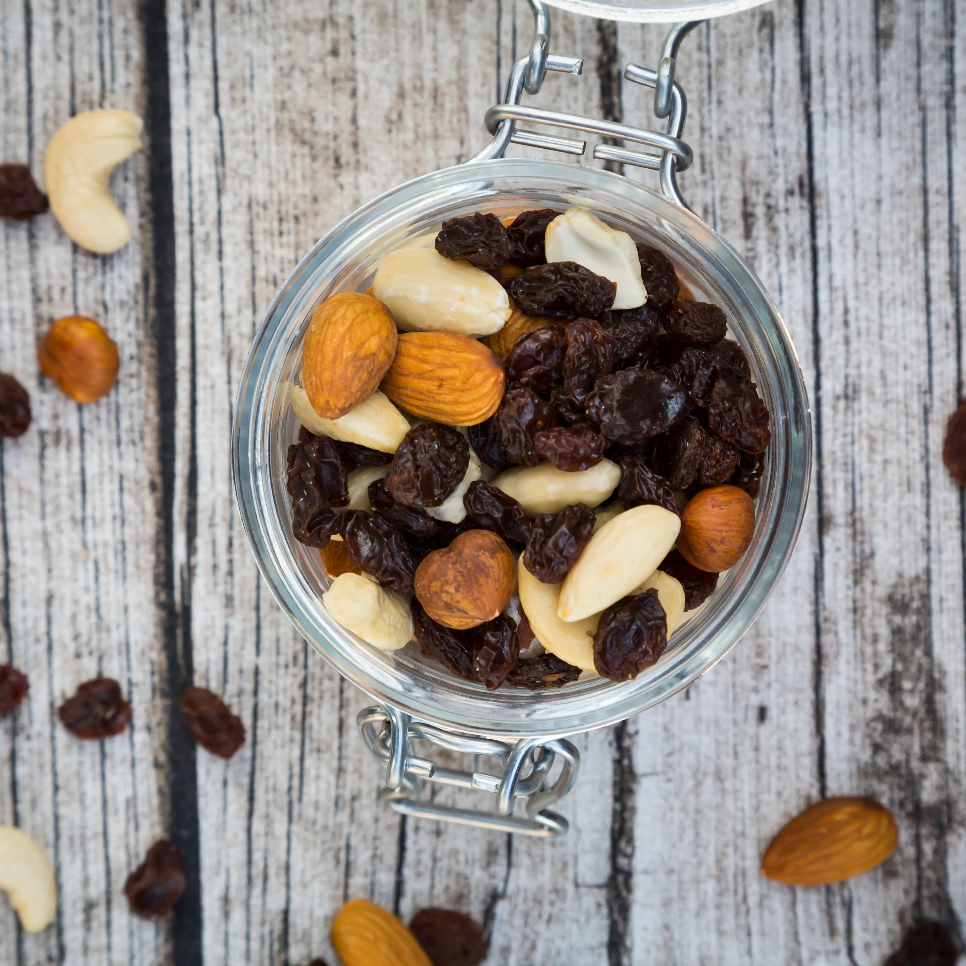 Mixed nuts and raisins in glass on wood