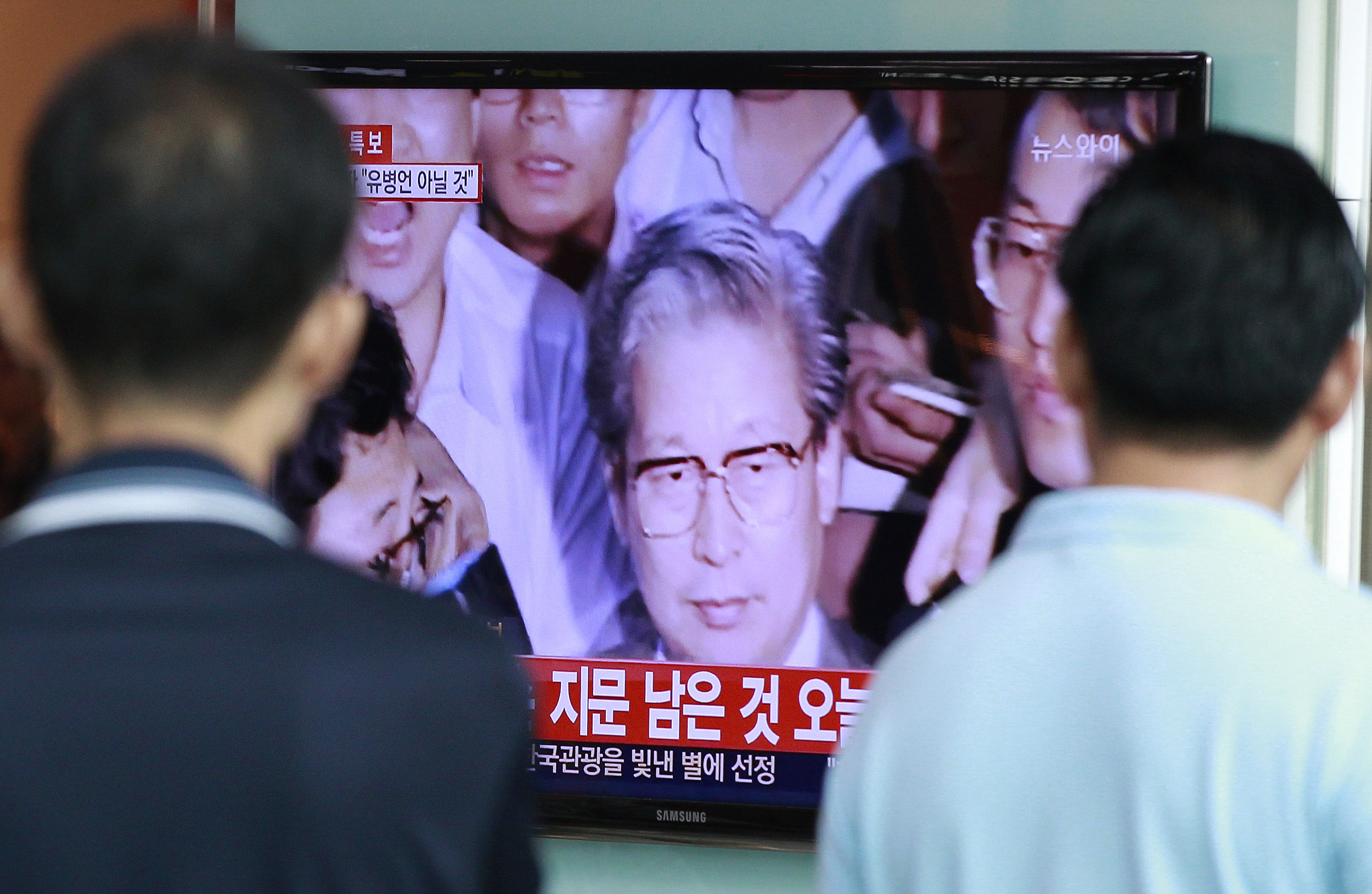 Passersby watch TV news showing Yoo Byung-eun, the fugitive owner of the sunken ferry Sewol, at Seoul Railway Station in Seoul on July 22, 2014.