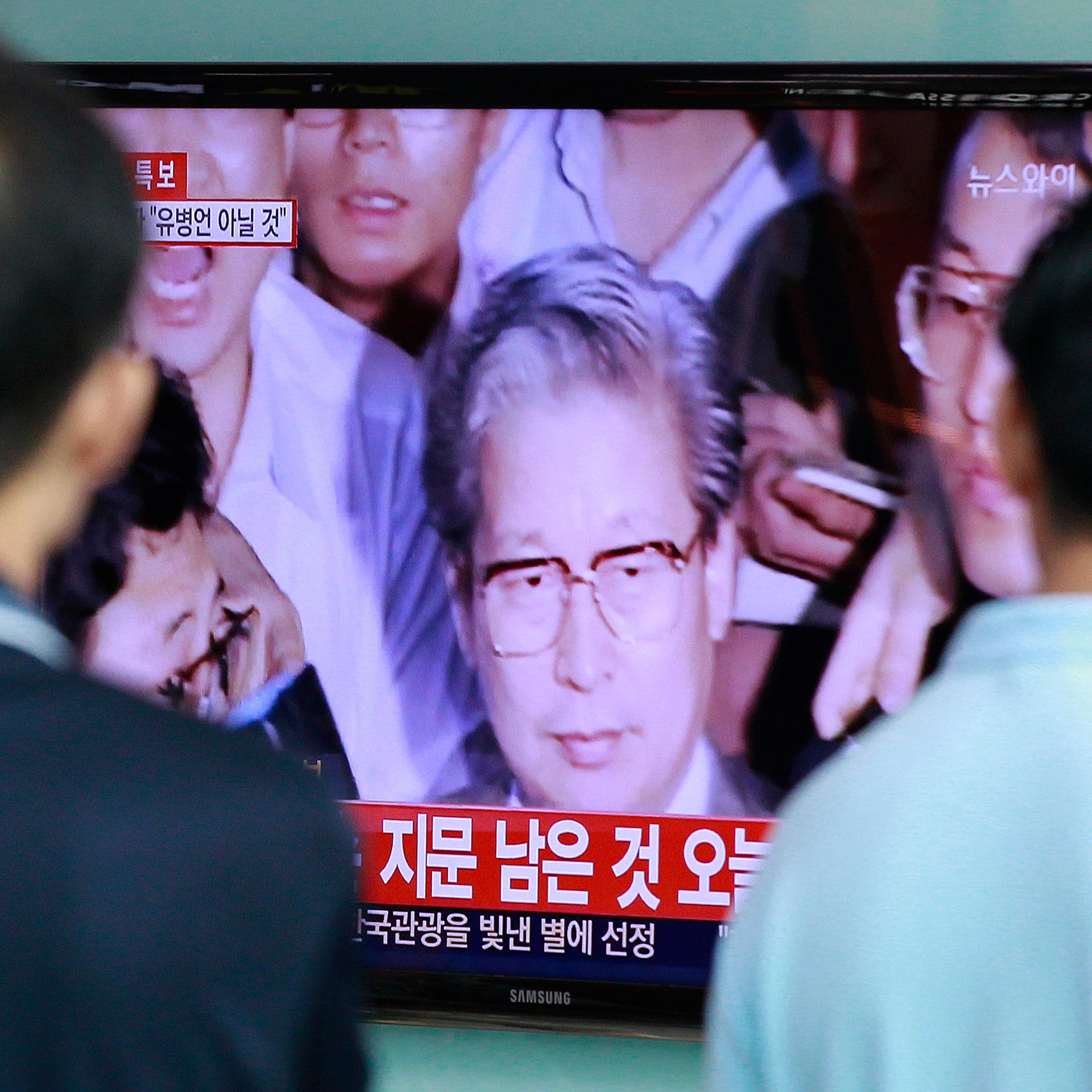 Passersby watch TV news showing Yoo Byung-eun, the fugitive owner of the sunken ferry Sewol, at Seoul Railway Station in Seoul on July 22, 2014.