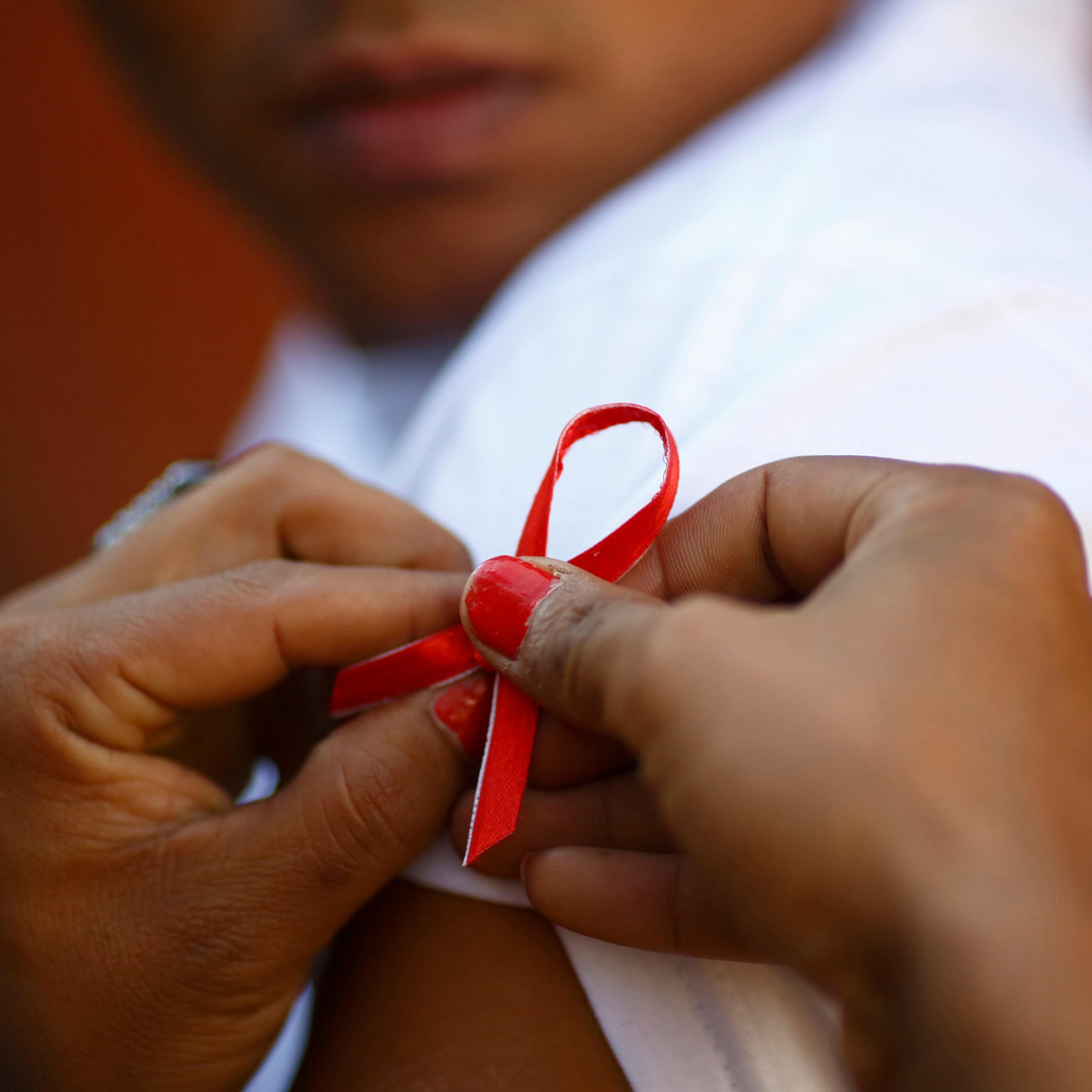 A red ribbon is put on the sleeves of a man by his friend to show support for people living with HIV during a program to raise awareness about AIDS on World AIDS Day in Kathmandu