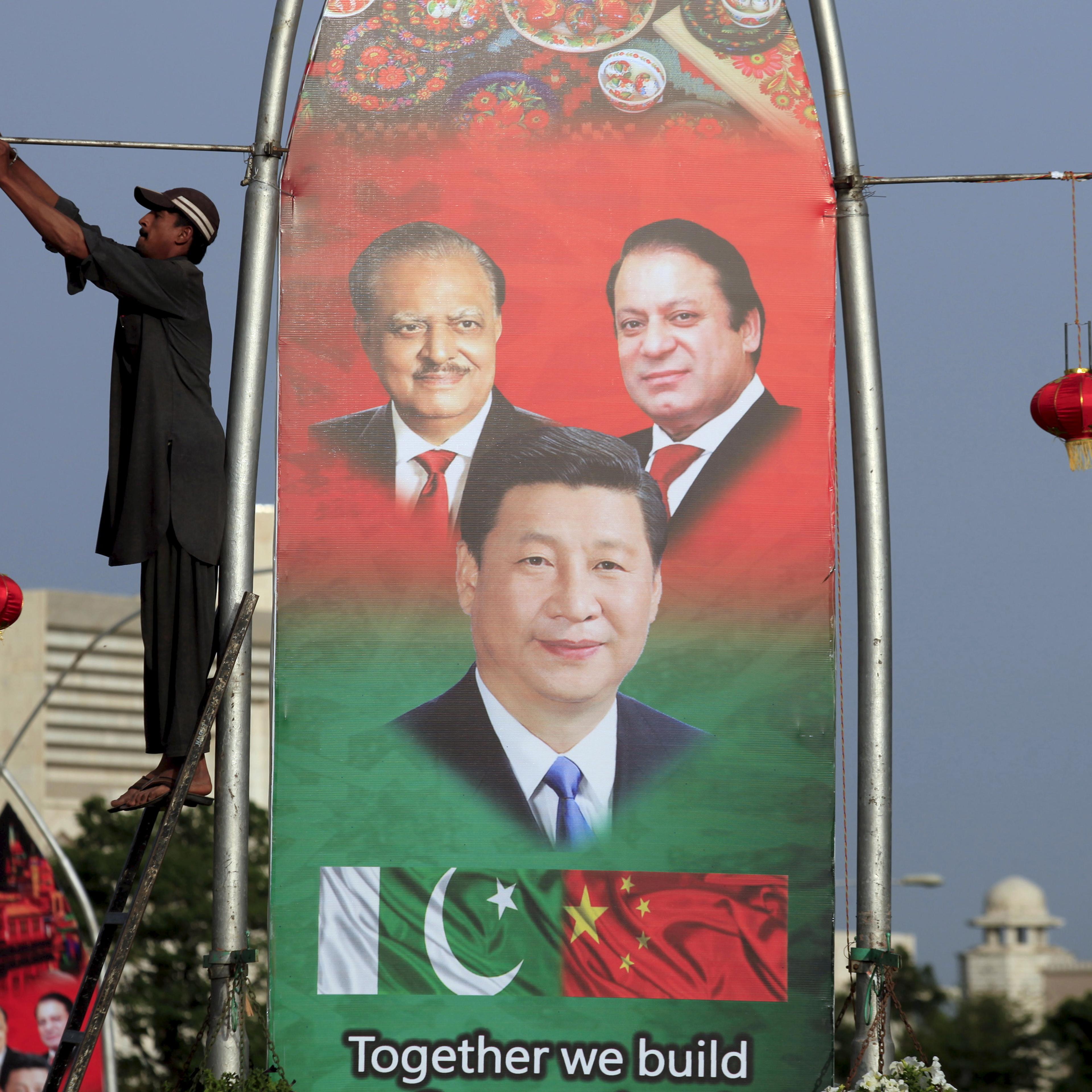 A man hangs decorations on a pole next to a banner showing Pakistan's President Hussain, China's President Xi and Pakistan's PM Sharif, ahead of Xi's visit to Islamabad