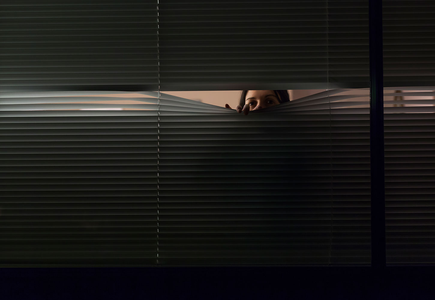Woman looking through venetian blinds