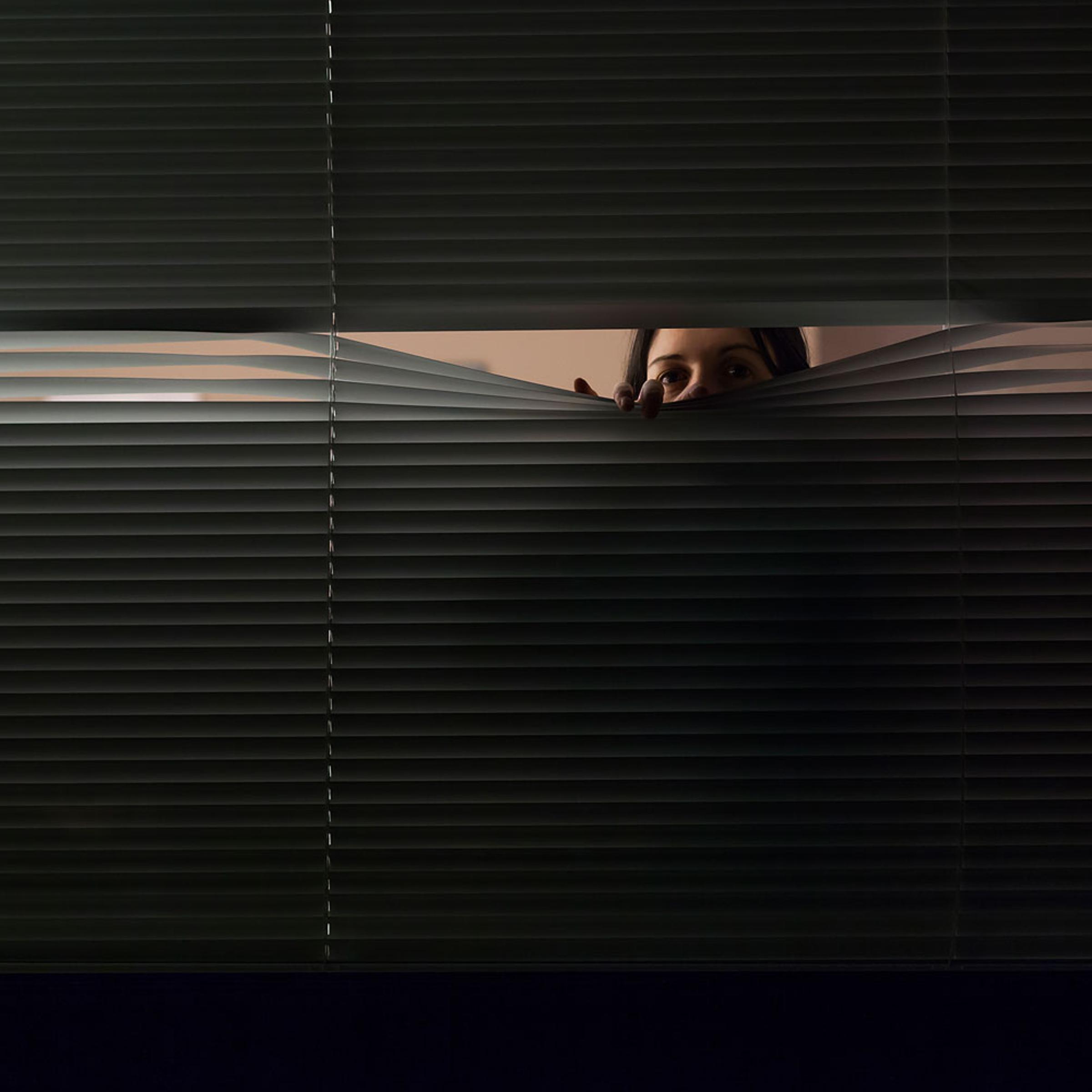 Woman looking through venetian blinds