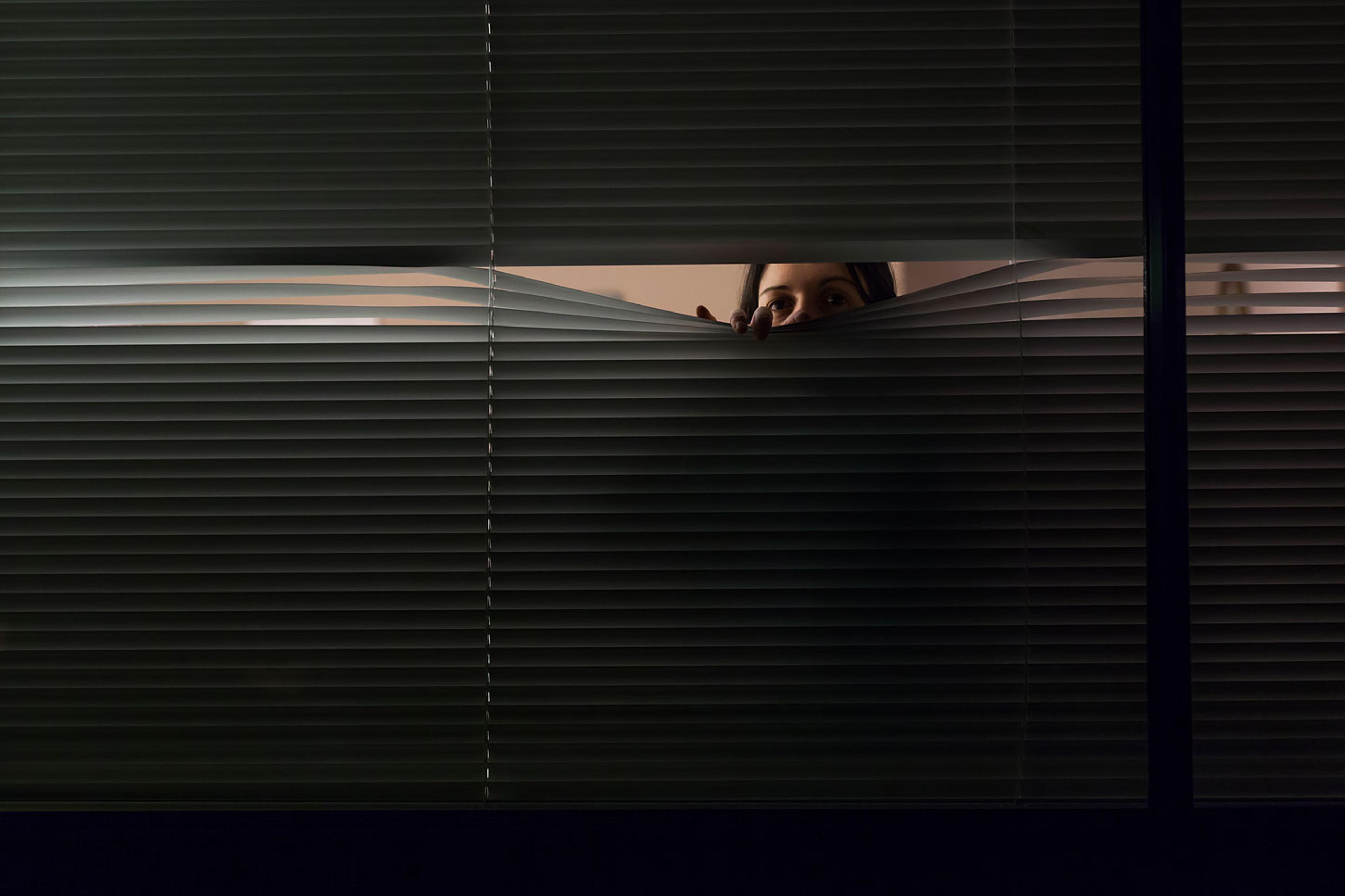 Woman looking through venetian blinds
