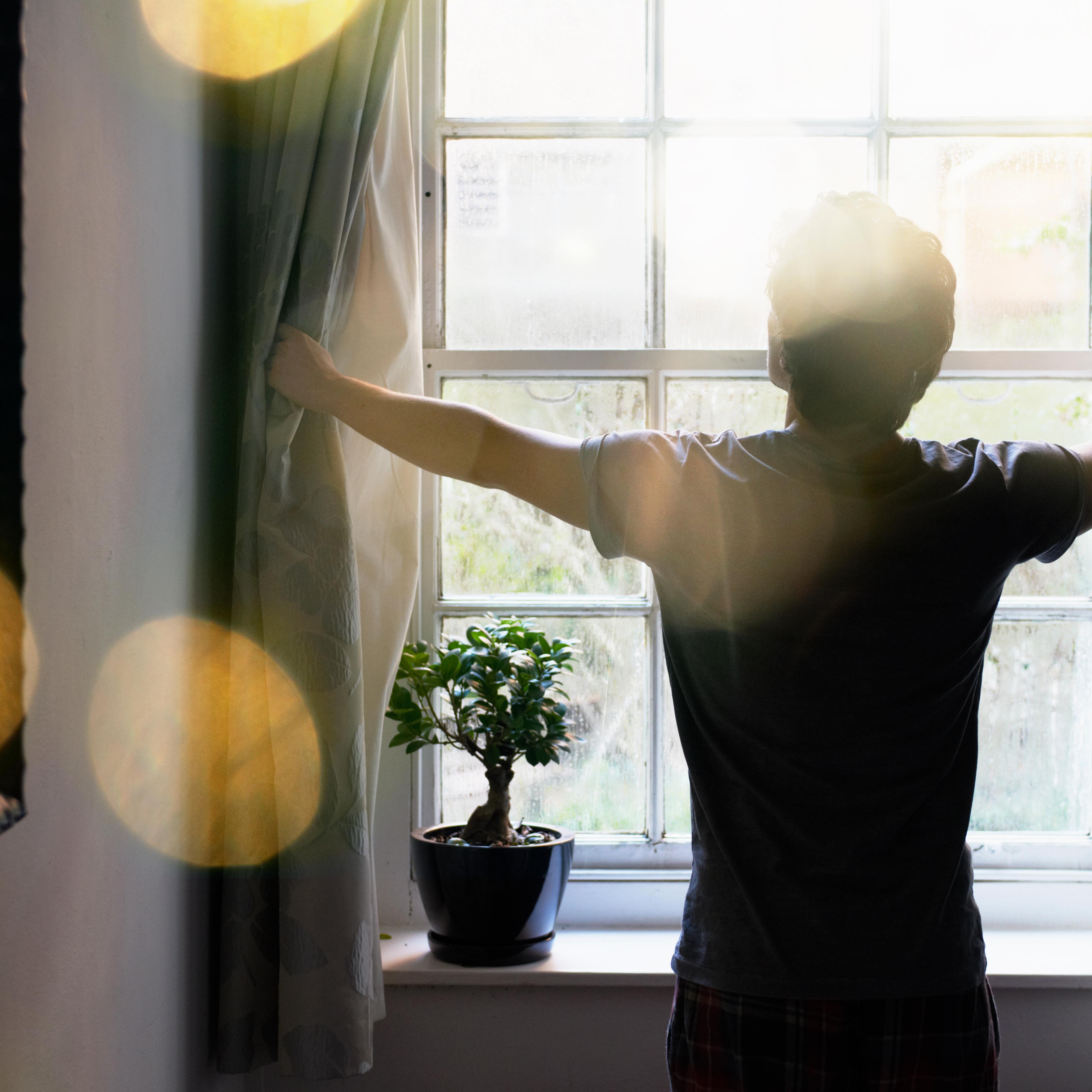 man opening curtains in the morning