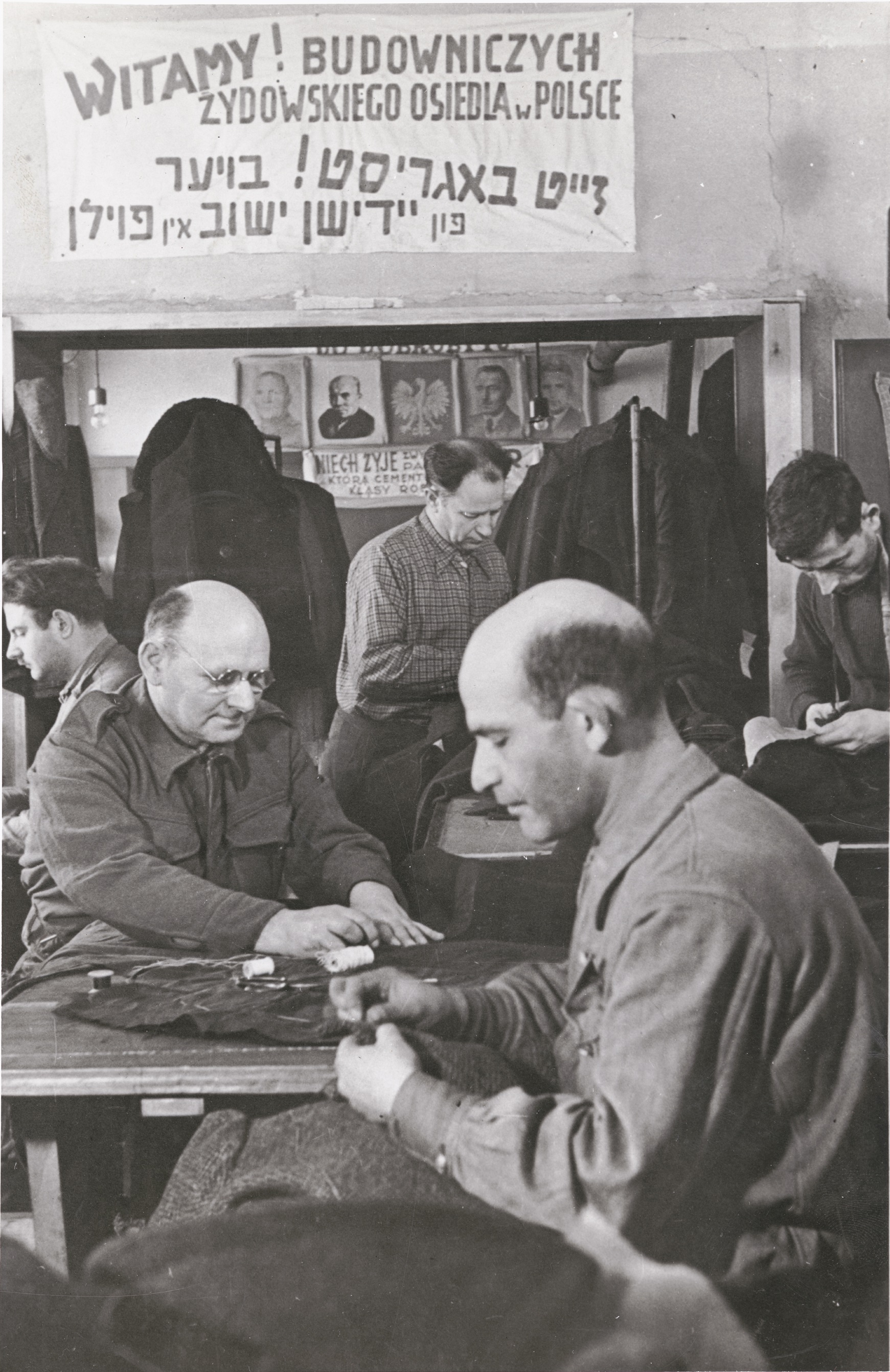 Polish Jews, among them repatriates, work in a tailor shop with a sign that reads in Polish and Yiddish, “Welcome! Building of the Jewish Community in Poland,” Dzieroniow, 1946. After World War II, Dzieroniow, in Lower Silesia, became a major Jewish resettlement center. Survivors went there to begin new lives. 