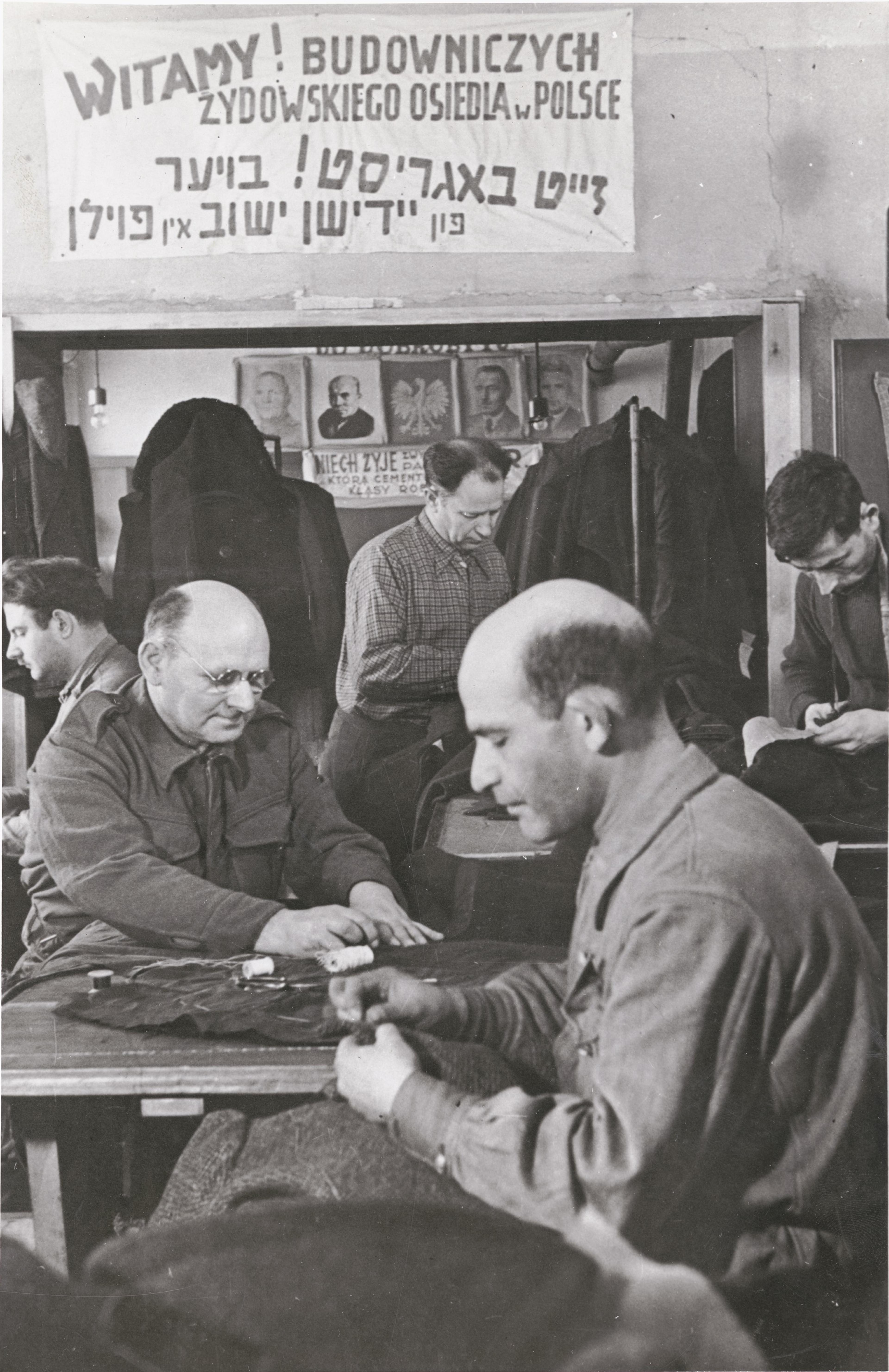 Polish Jews, among them repatriates, work in a tailor shop with a sign that reads in Polish and Yiddish, “Welcome! Building of the Jewish Community in Poland,” Dzieroniow, 1946. After World War II, Dzieroniow, in Lower Silesia, became a major Jewish resettlement center. Survivors went there to begin new lives.