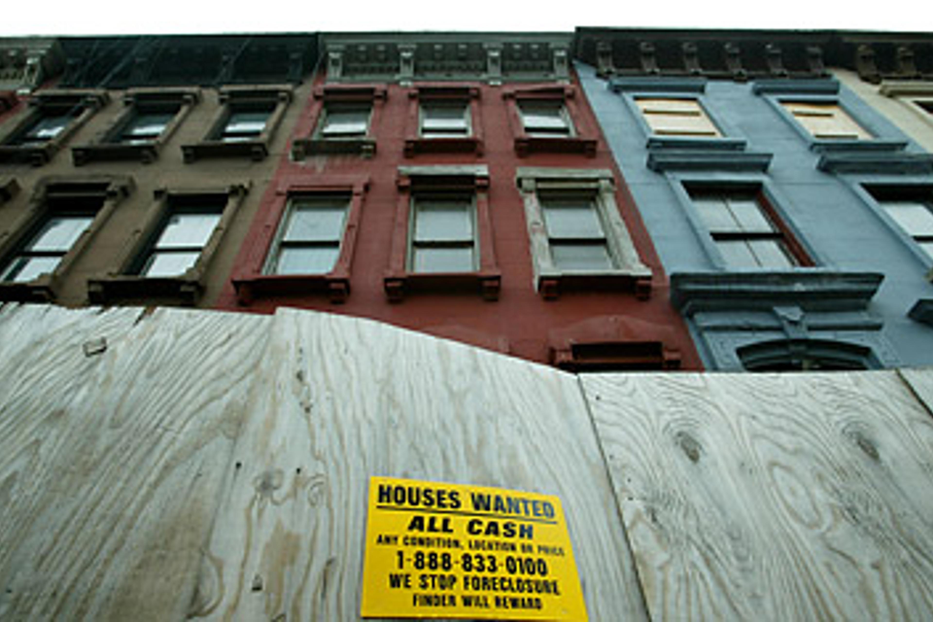 A sign advertising for "Houses Wanted" stands on a temporary wall in front of row houses in the Harlem neighborhood of New York City.