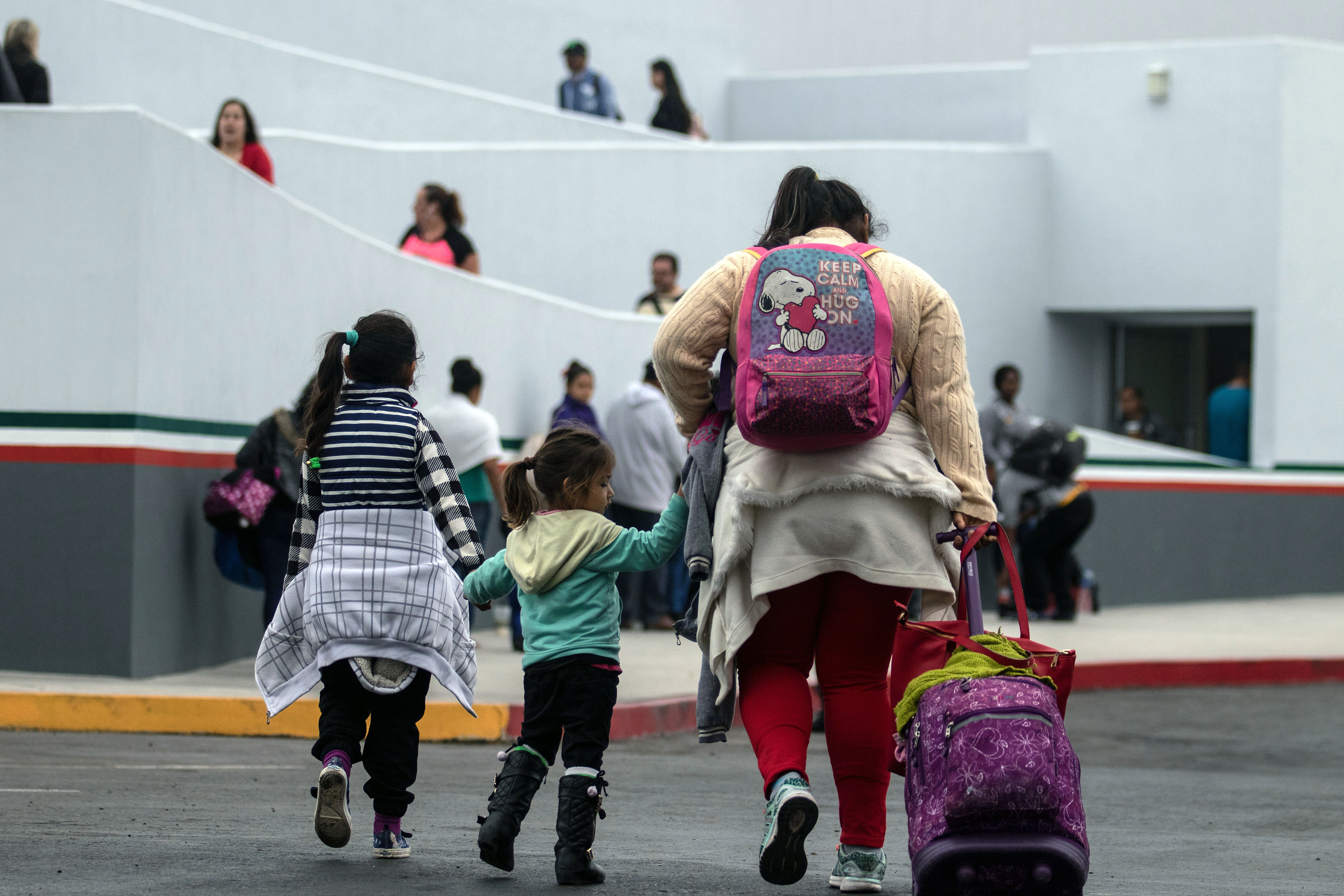 A mother and two children walk with bags