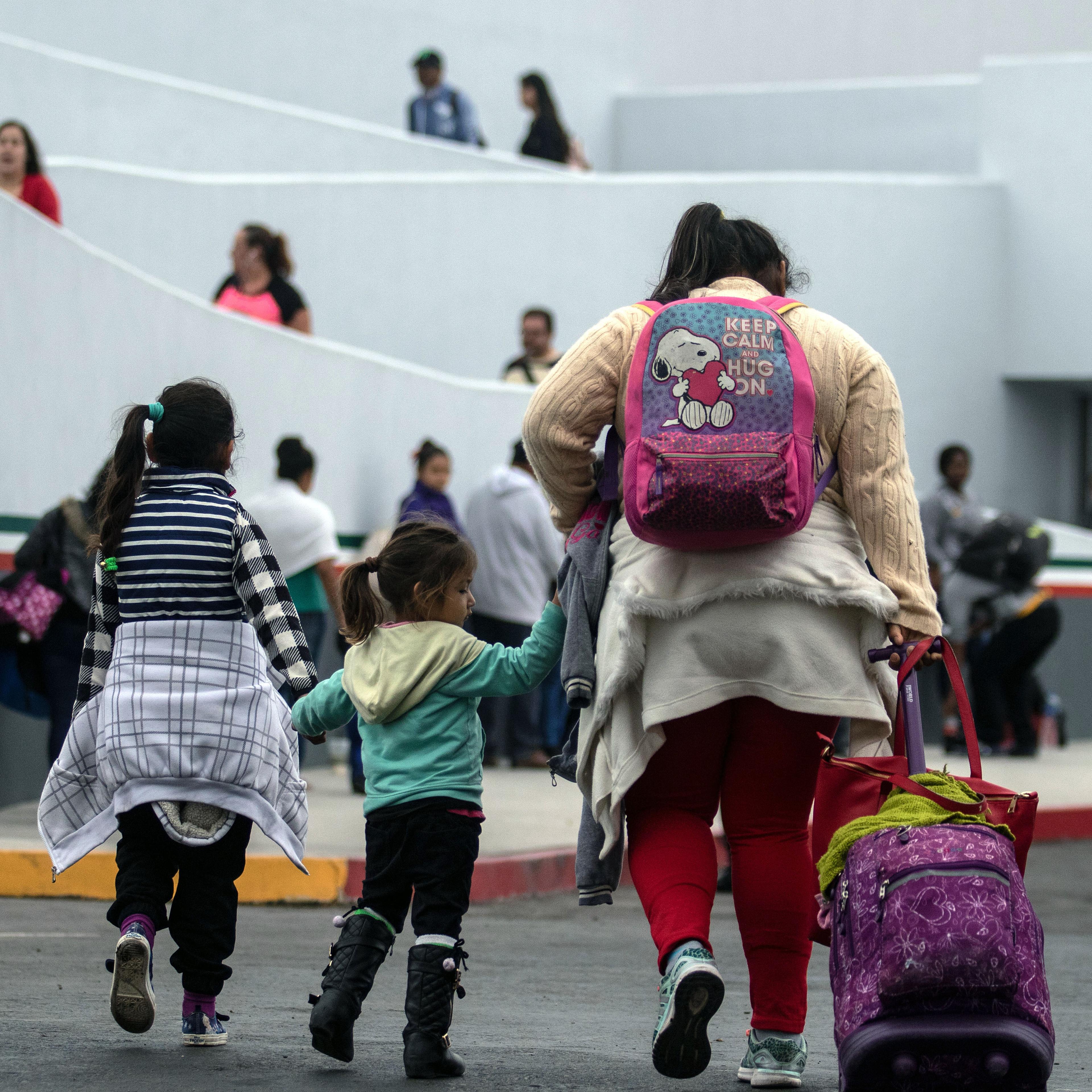 A mother and two children walk with bags