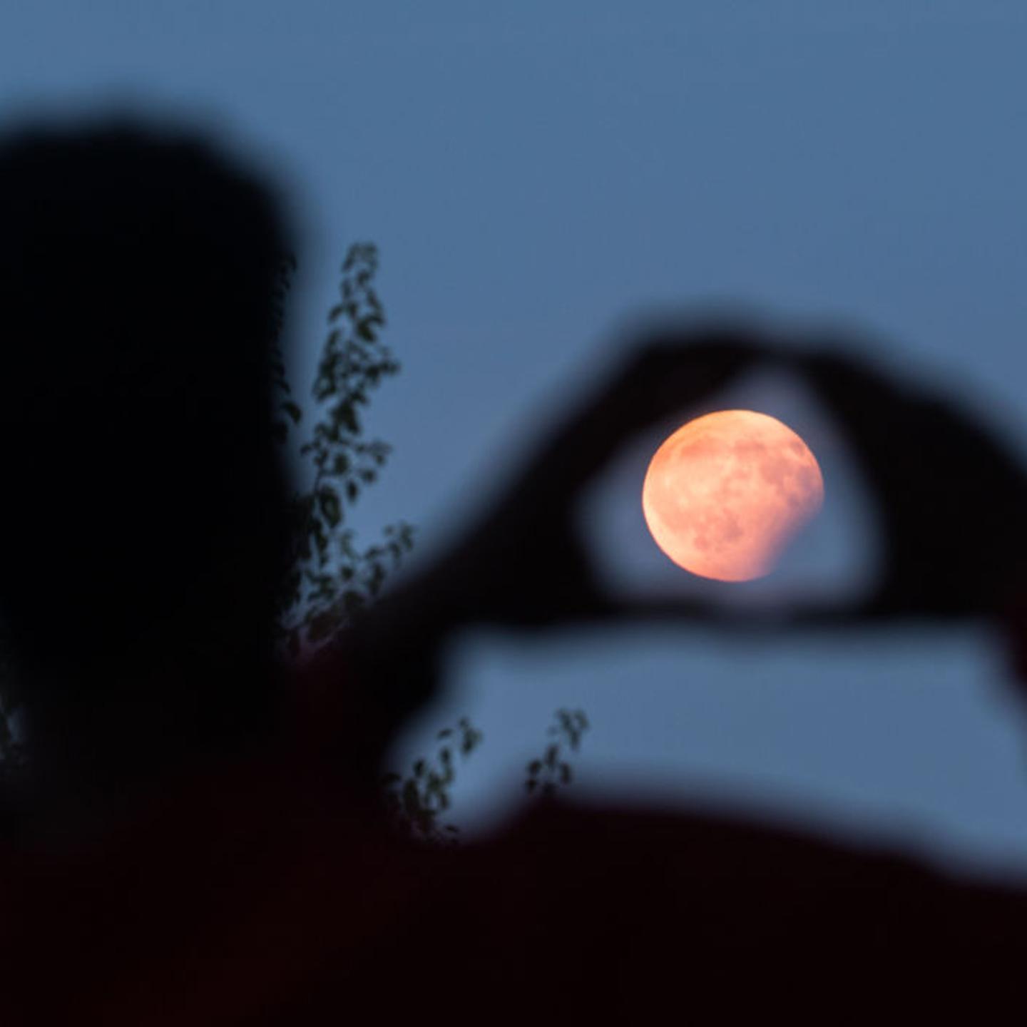 A man frames with his hands the moon standing in a partial lunar eclipse on August 7, 2017 in Frankfurt am Main, western Germany.